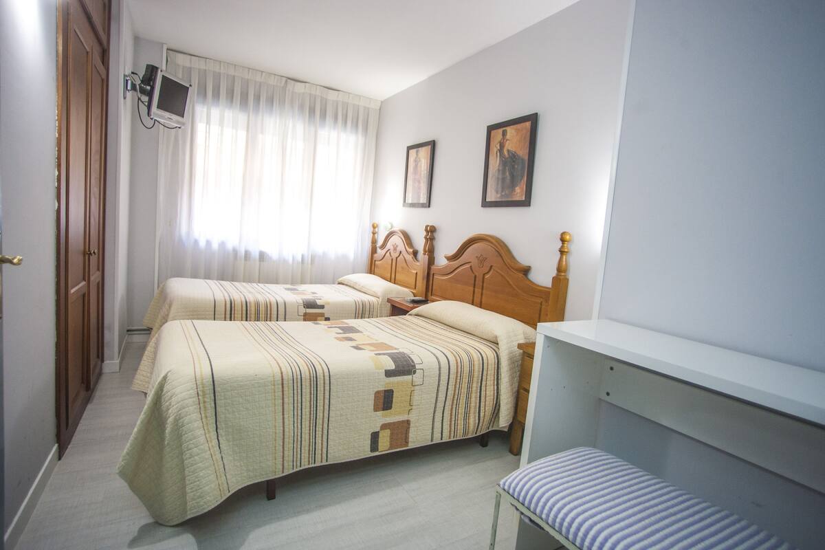 A hotel room with two beds, a television, and a bench.