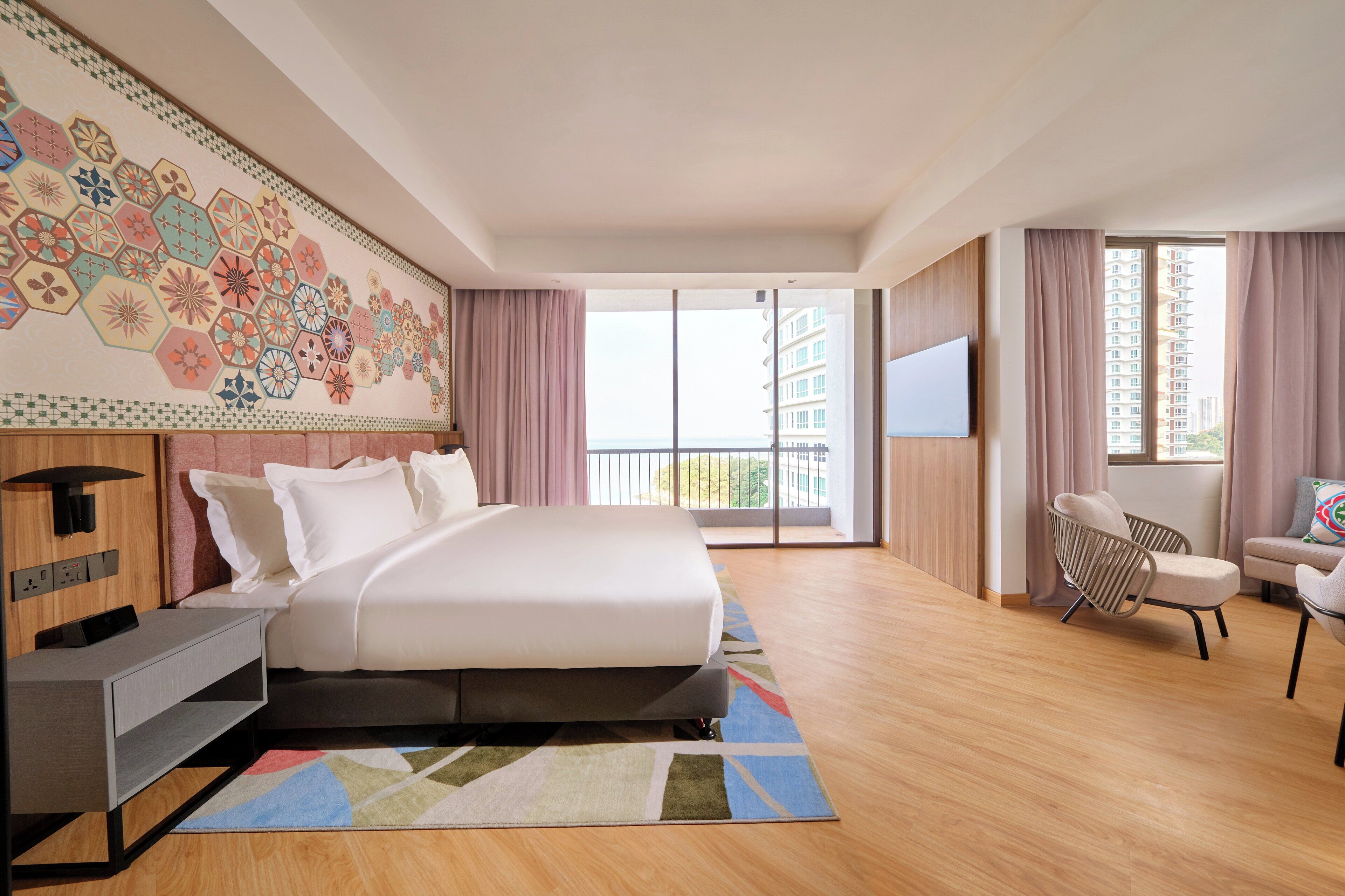 Ein modernes Hotelzimmer mit einem großen Bett, einem Schreibtisch, einem Stuhl und einem Fernseher. Das Zimmer verfügt über einen Balkon mit Blick auf die Stadt.