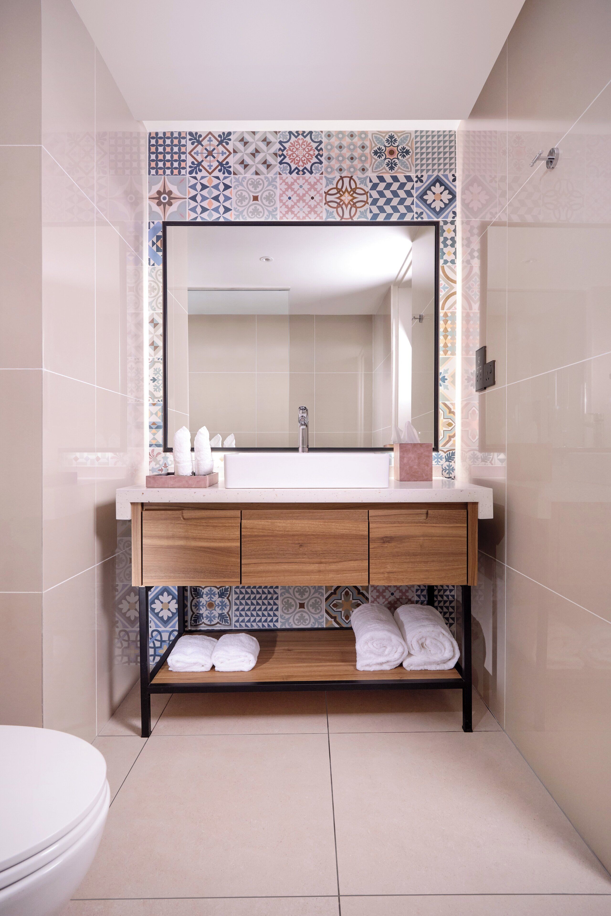 A bathroom with a white sink, wooden vanity, and a tiled backsplash.