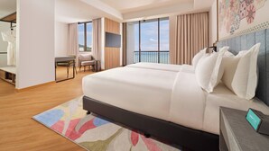 A hotel room with a large bed, a desk, and a chair. There is a balcony with a view of the ocean. - M Social Resort Penang (George Town)