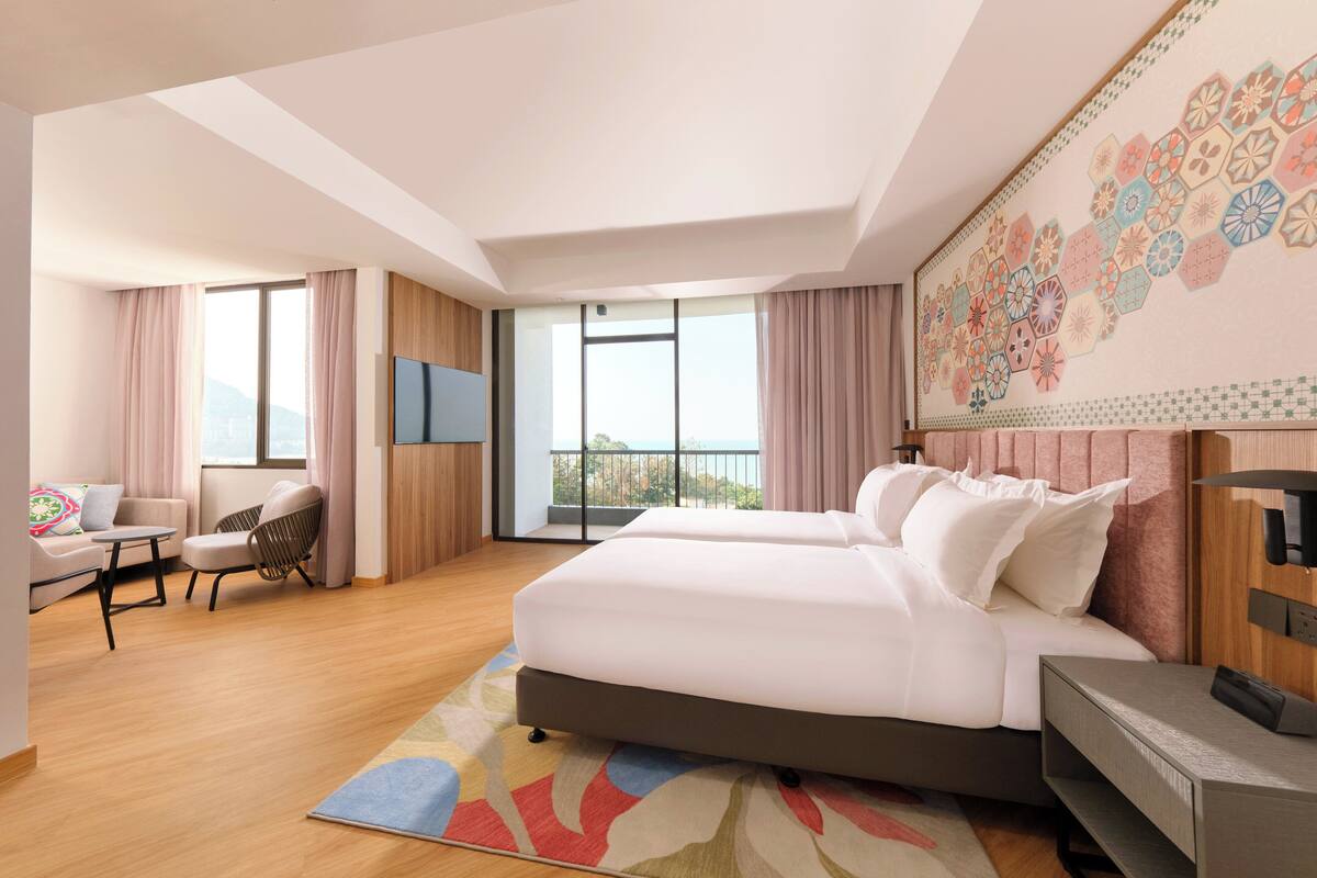 A modern hotel room with a large bed, a sofa, a TV, and a balcony with a view.