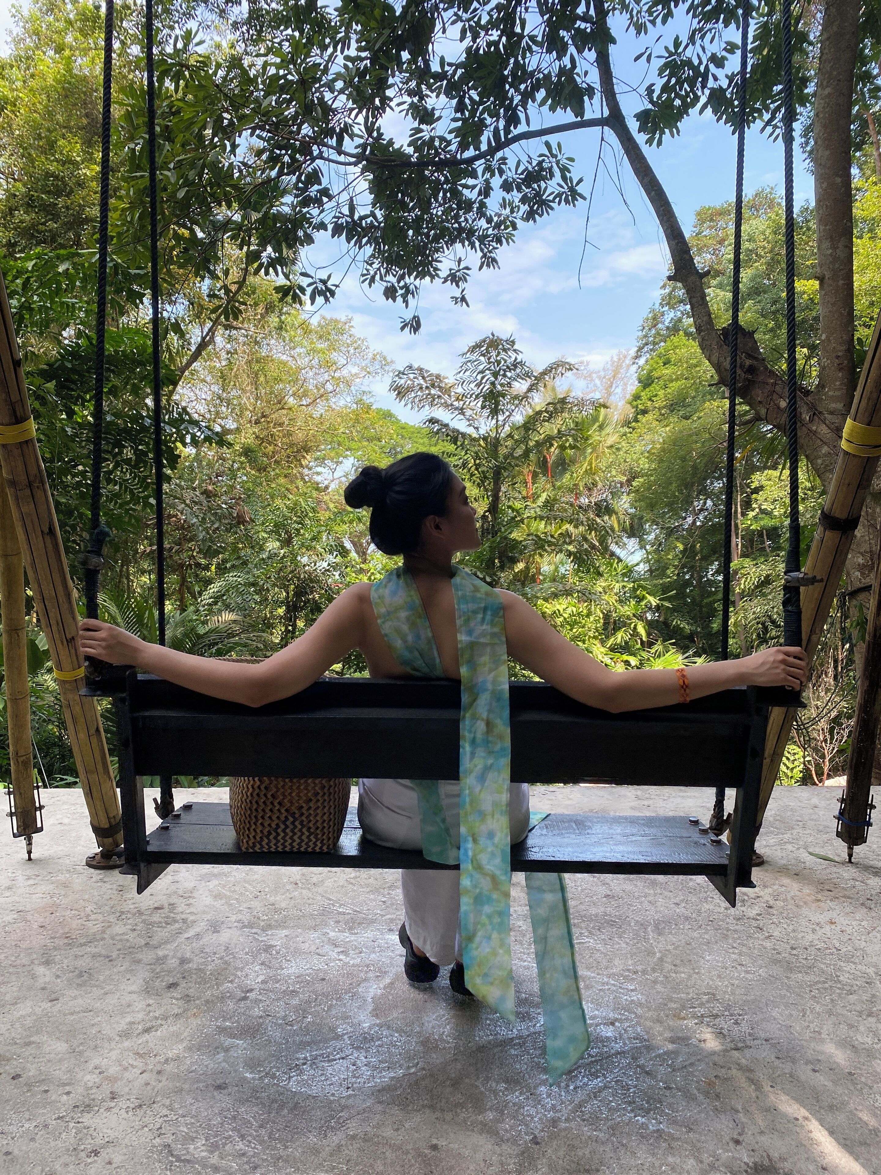 A person sitting on a swing with a view of trees and a clear sky.