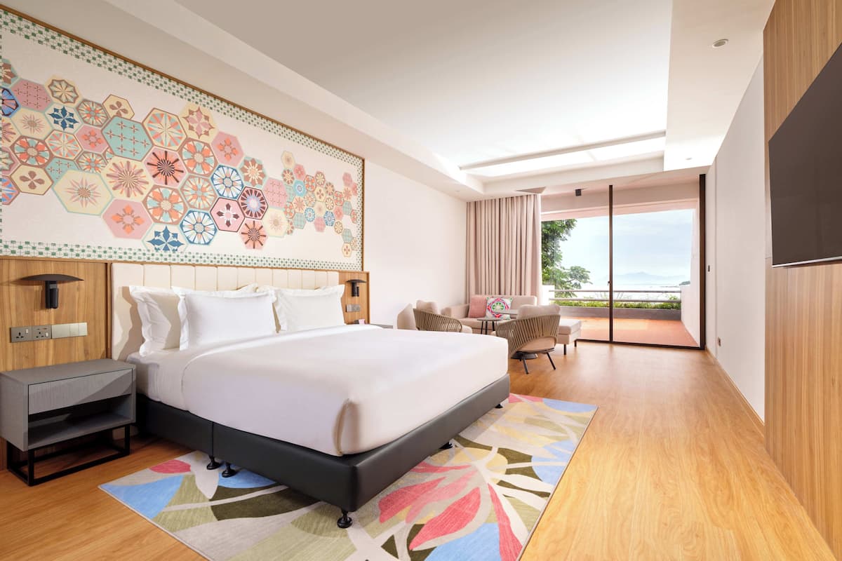 A modern hotel room with a large bed, a desk, a chair, and a view of the outdoors.