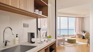 A modern kitchen with a large sink, a coffee maker, and a bottle of hand soap. There is a wooden cabinet above the sink and a window with a view of the ocean. - M Social Resort Penang (George Town)