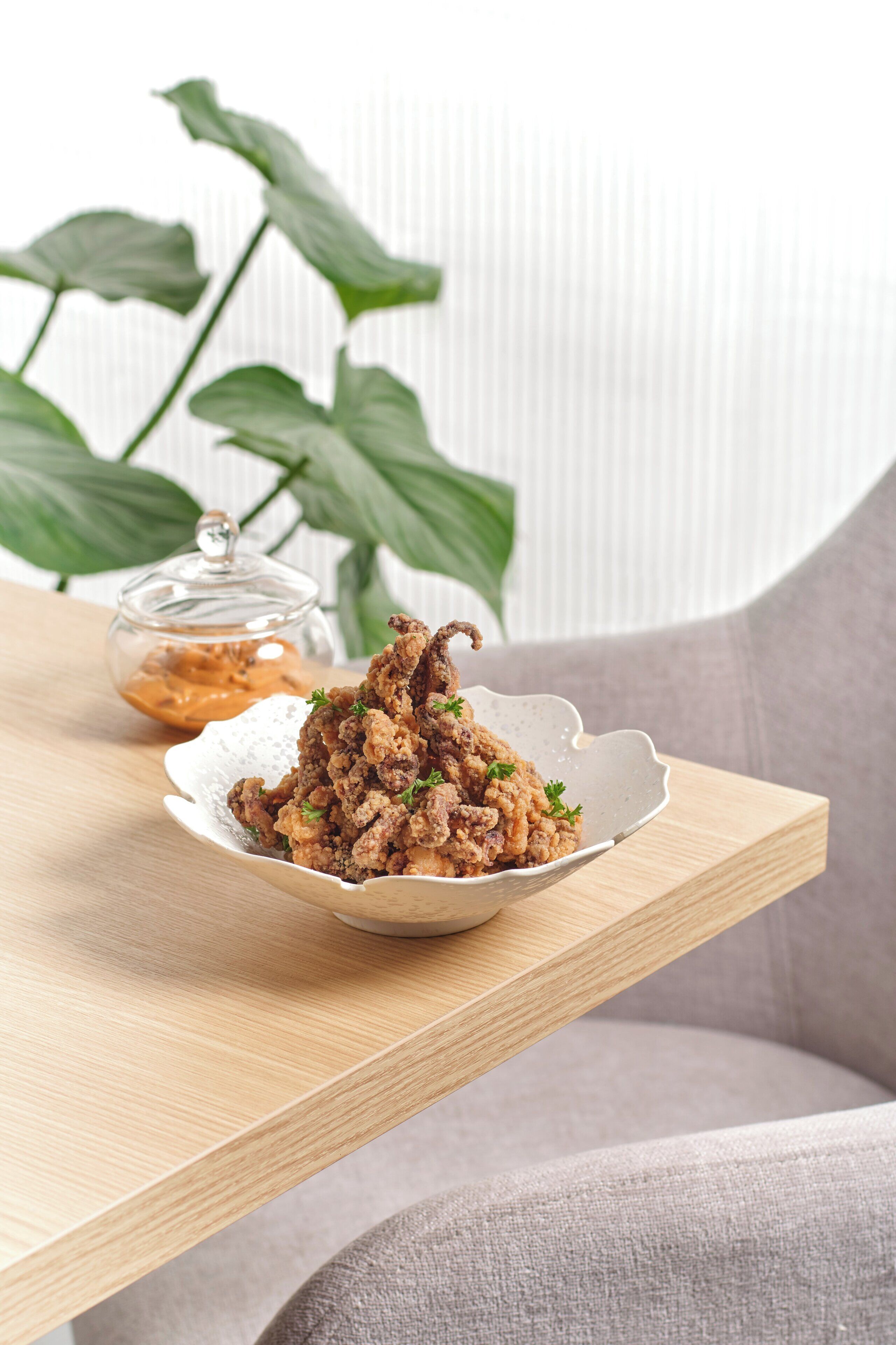 A plate of fried chicken on a wooden table with a glass jar of sauce in the background.