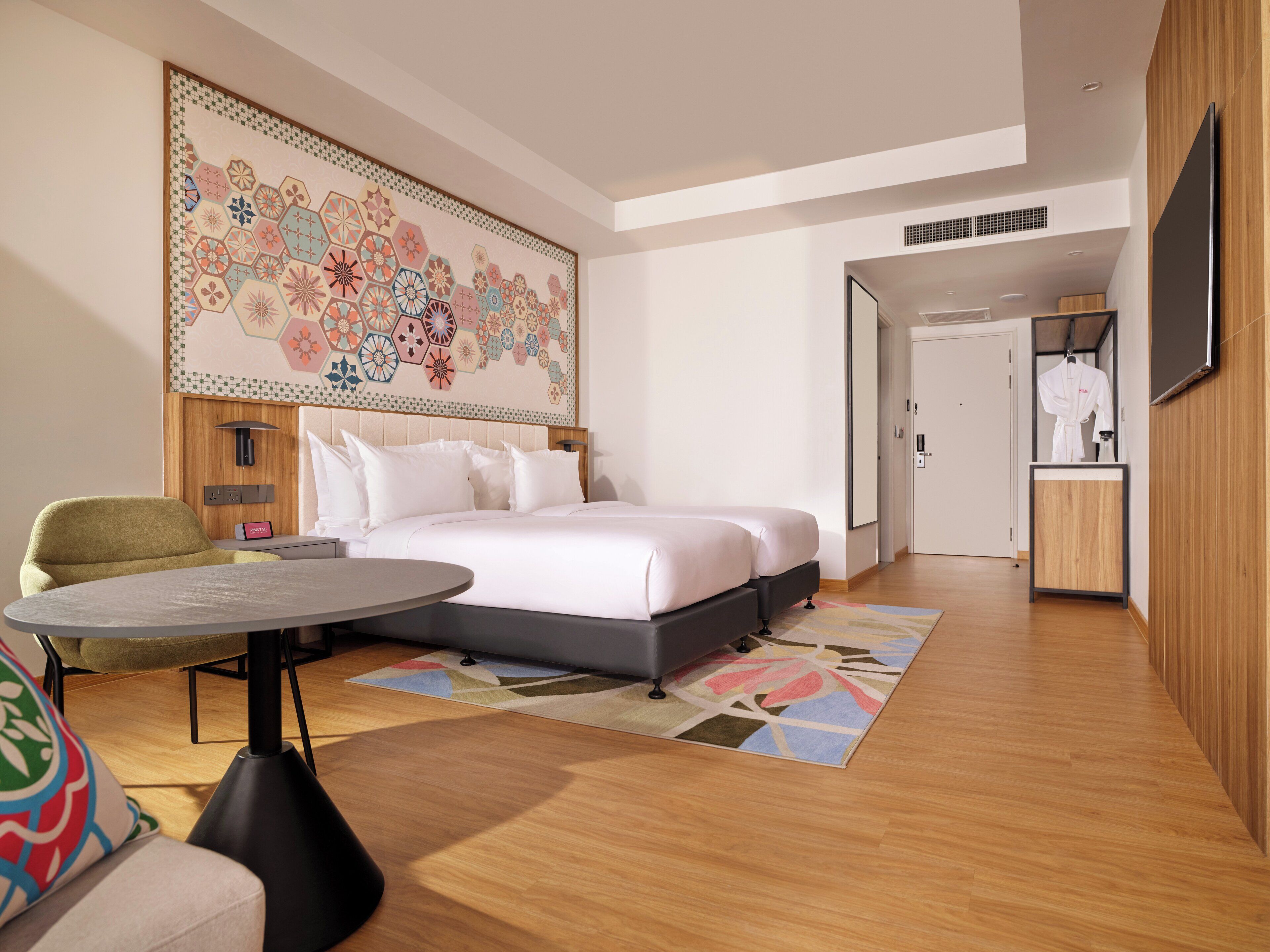 A modern hotel room with a large bed, a desk, a chair, and a large decorative wall piece.