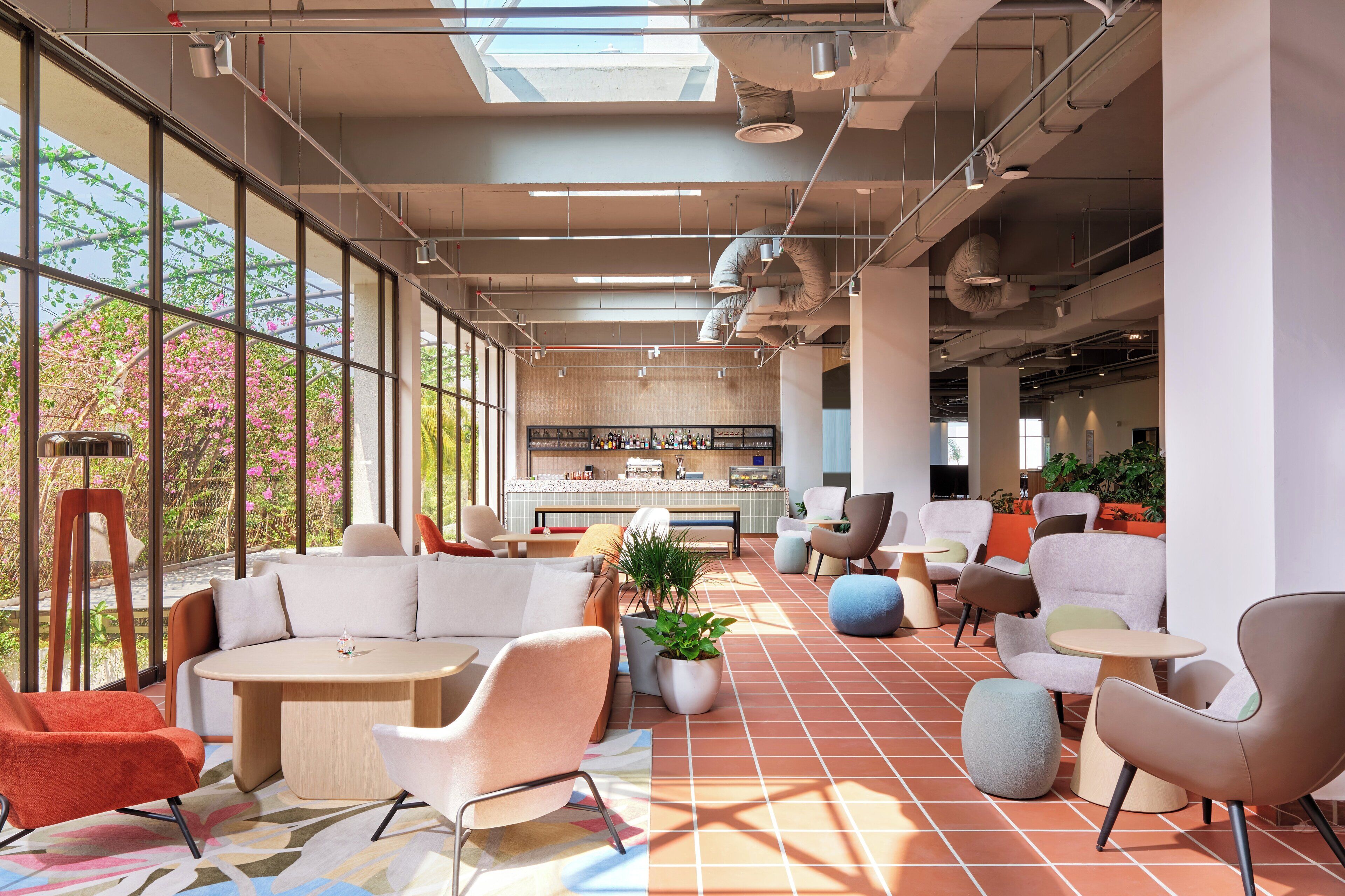 A modern indoor space with large windows, a variety of seating arrangements, and a visible kitchen area.