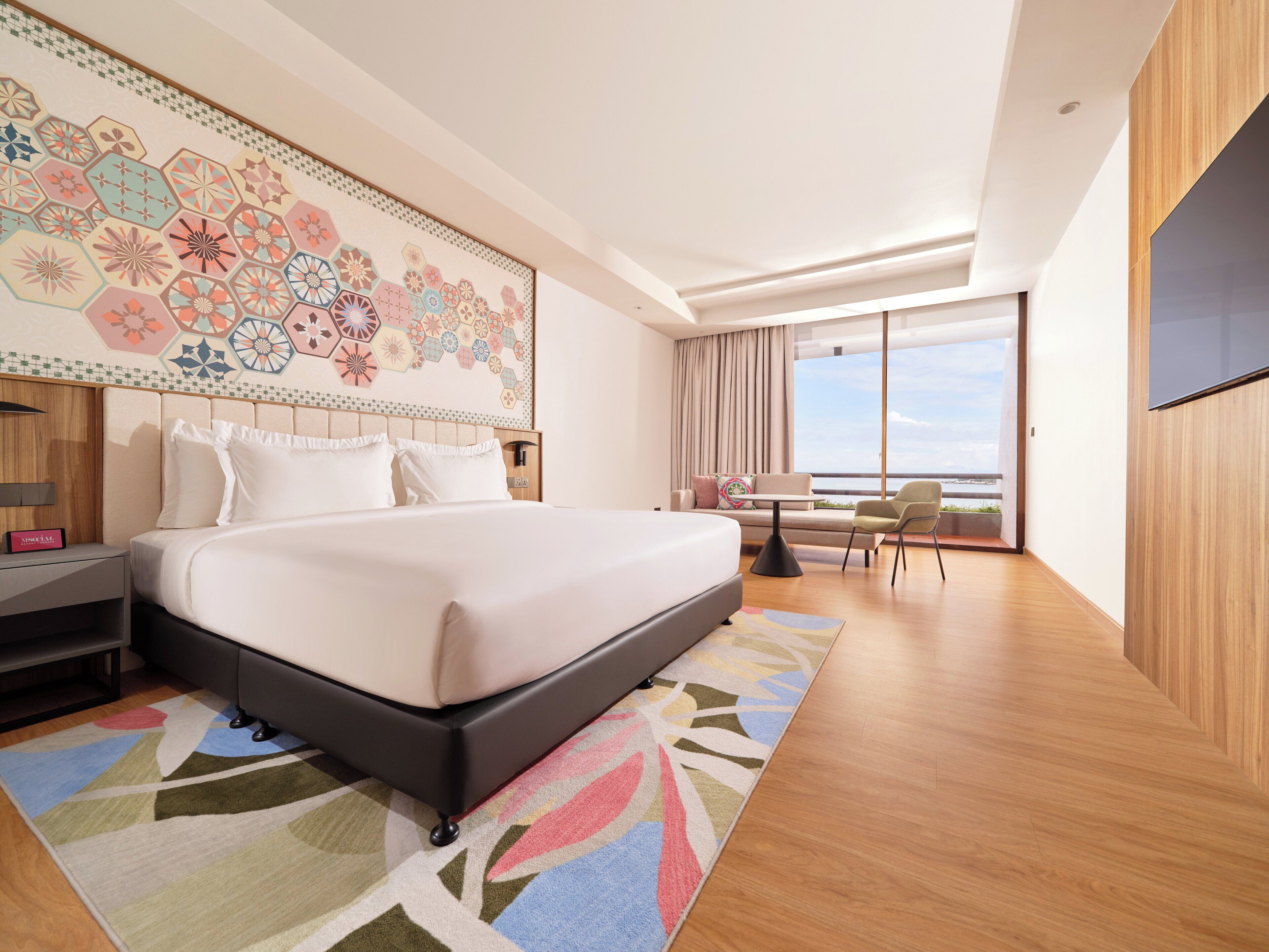 A modern hotel room with a large bed, a desk, and a view of the sea.