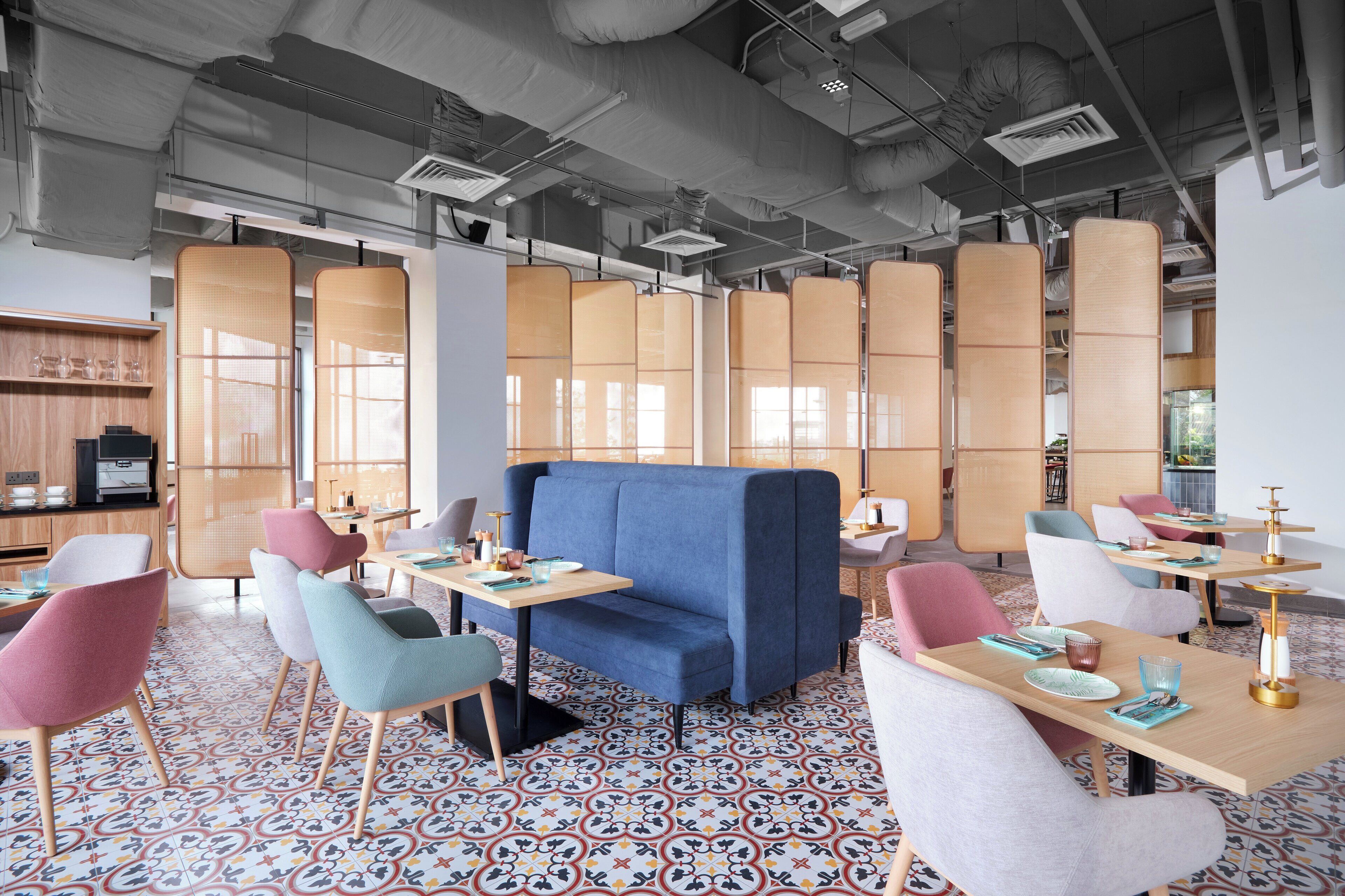 A modern dining area with a blue sofa, colorful chairs, and patterned floor tiles.