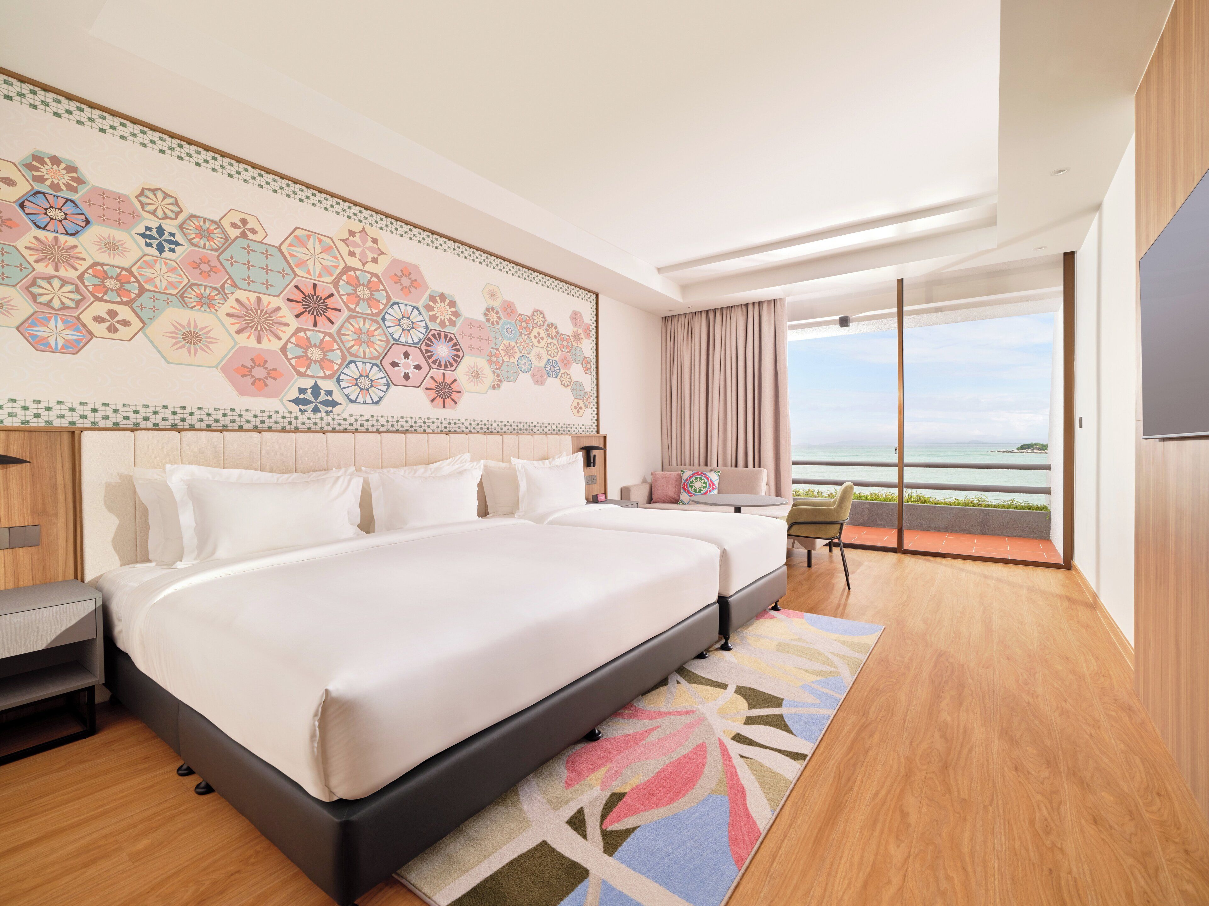 A modern hotel room with a large bed, a view of the sea, and a decorative wall.