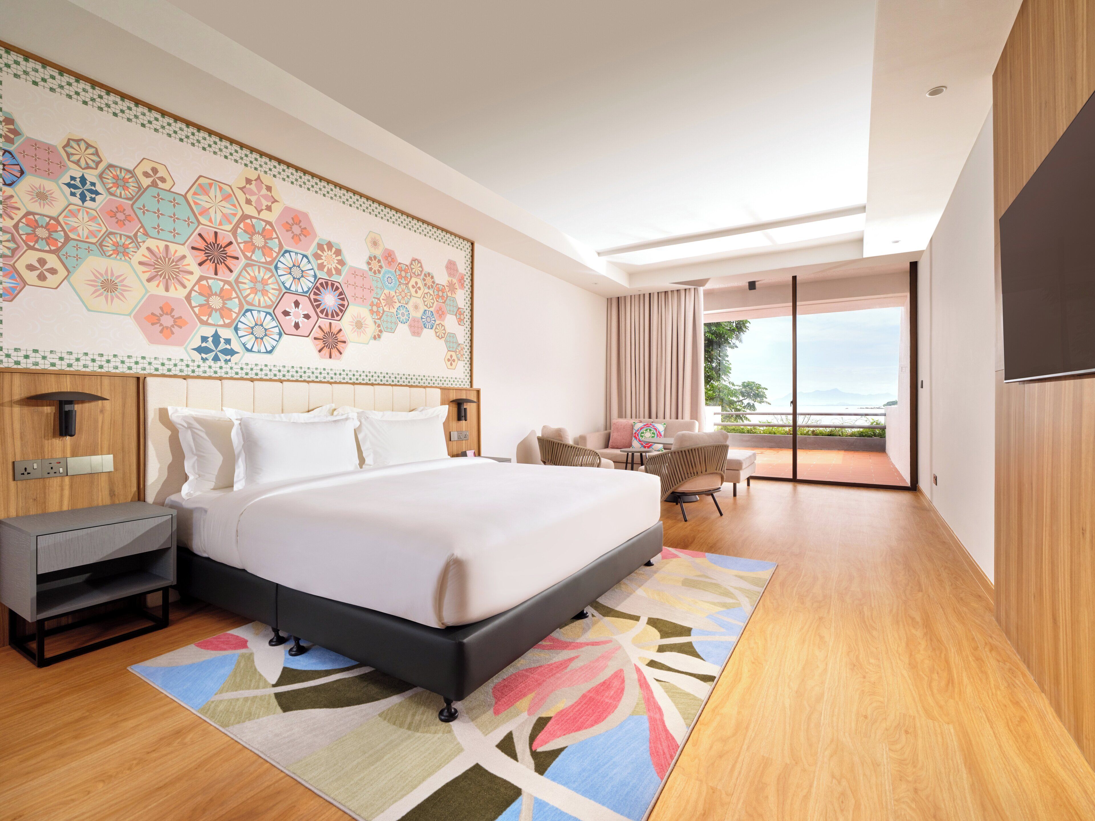 Een moderne hotelkamer met een groot bed, een bureau, een stoel en uitzicht op het omliggende landschap.