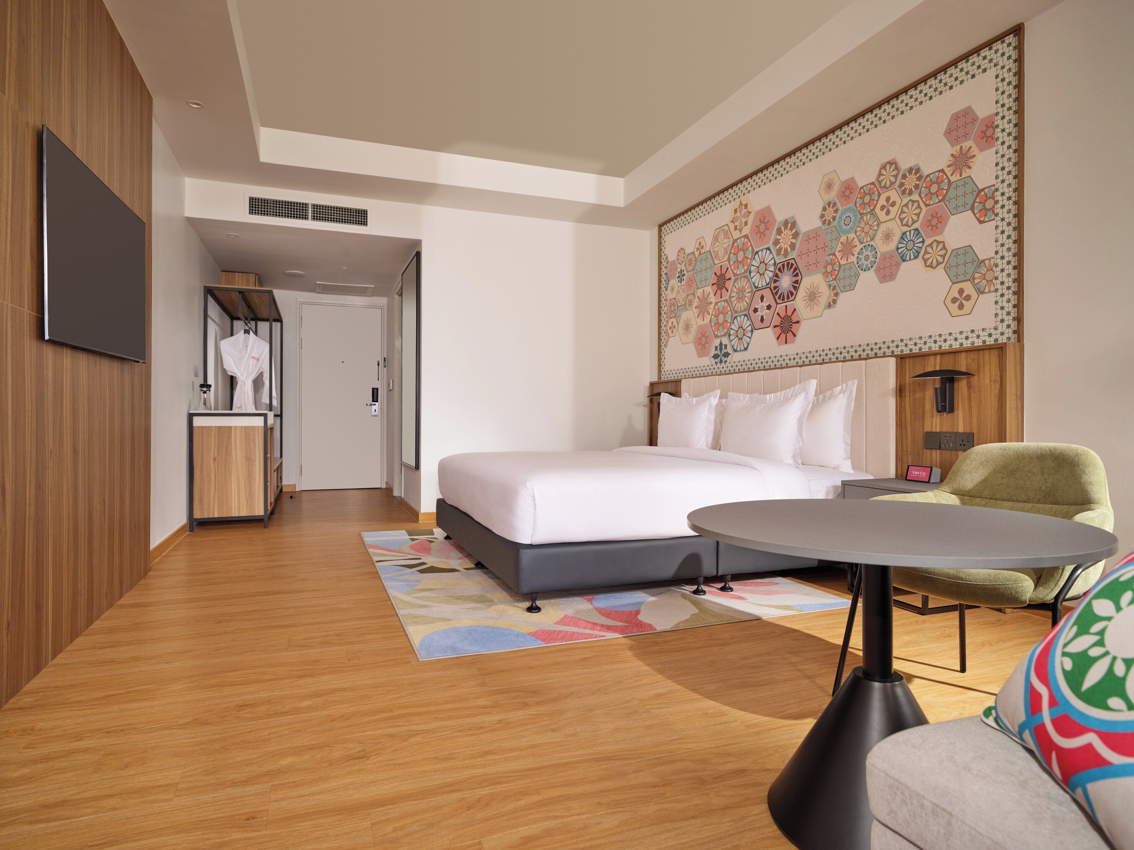 A modern hotel room with a large bed, a desk, and a colorful wall tapestry.