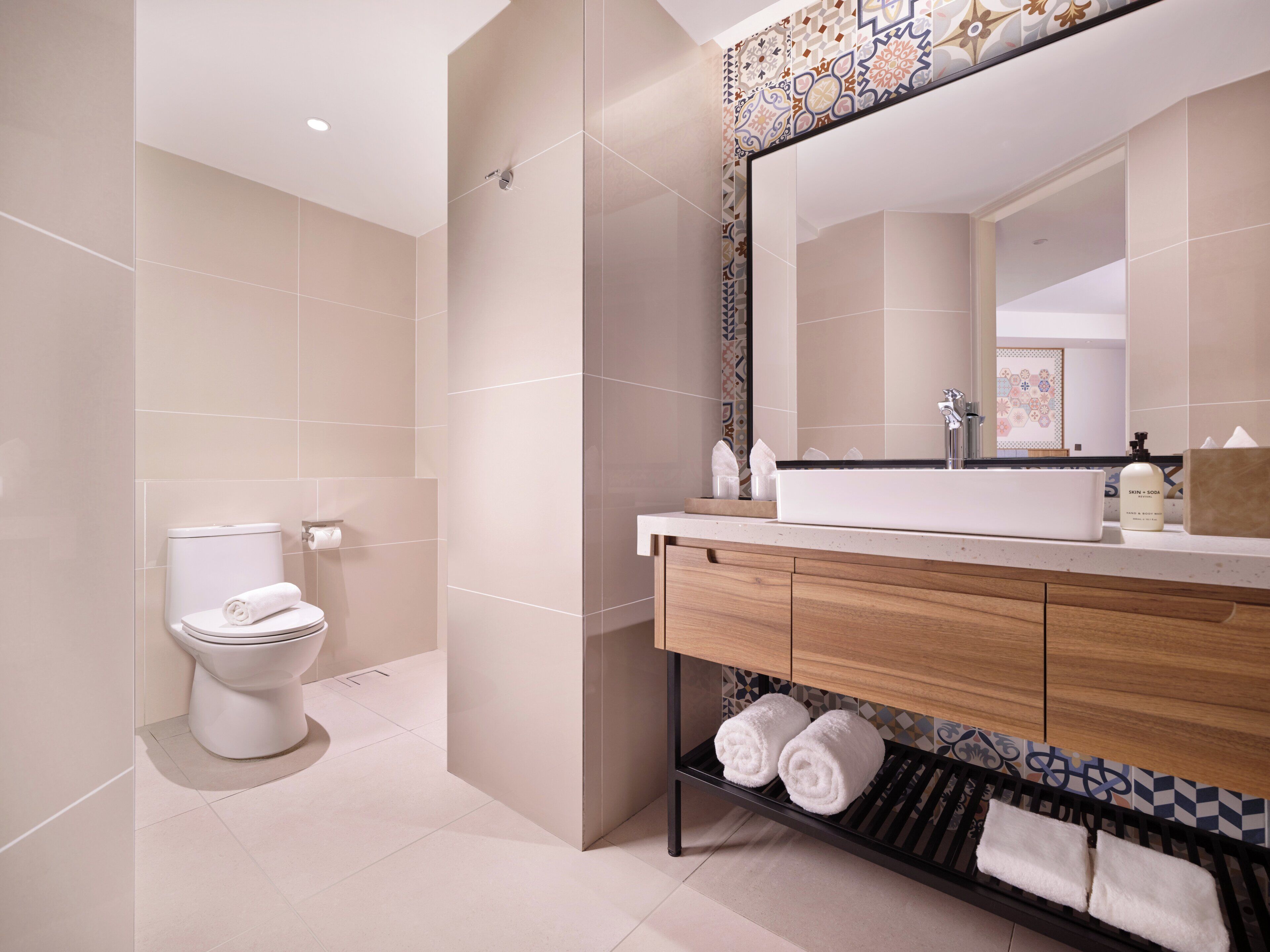 A modern bathroom with a toilet, sink, and mirror. There are towels on a rack and a bottle of soap on the sink.