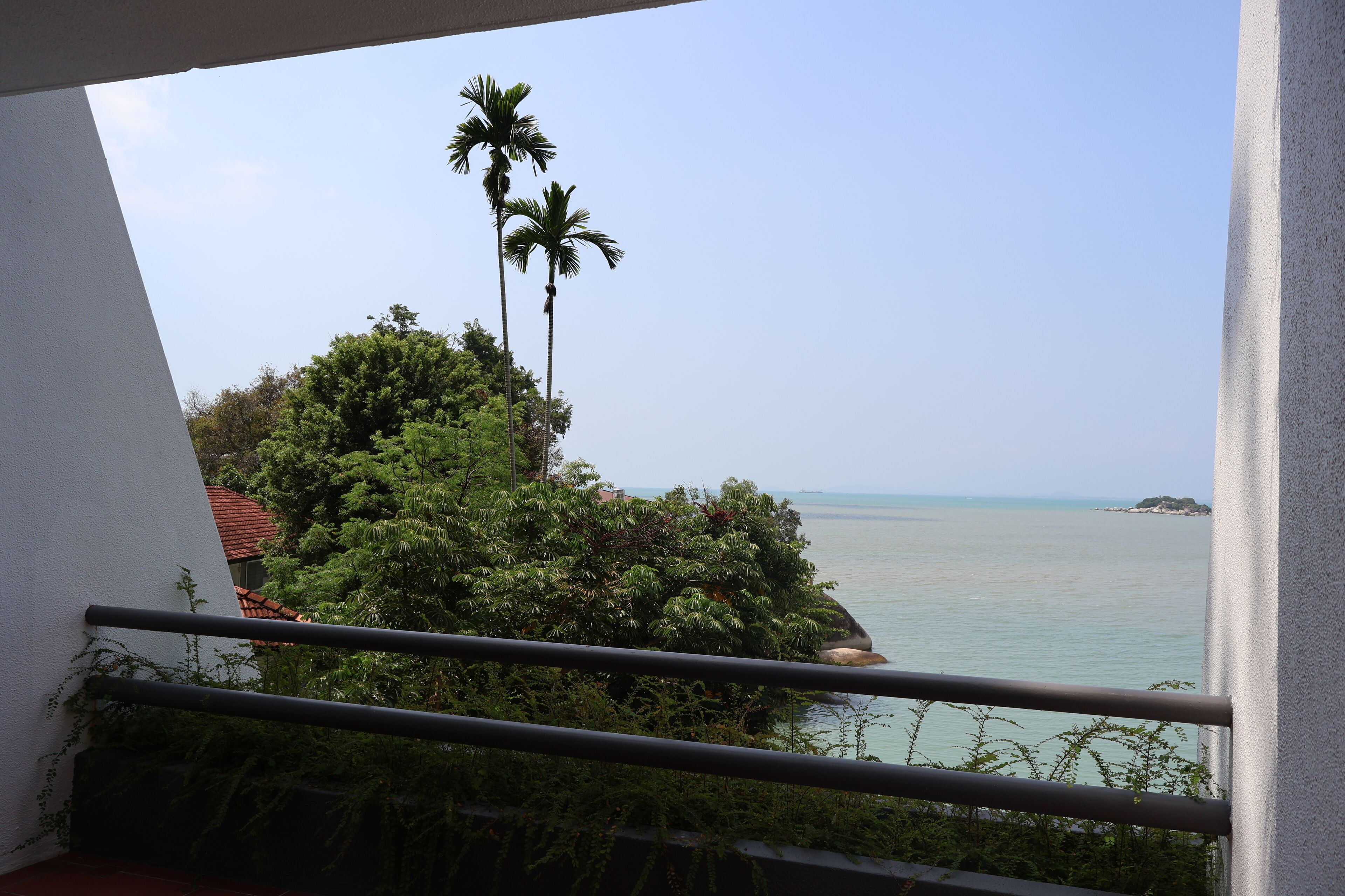 Ein Balkon mit Blick auf das Meer, Palmen und eine ferne Insel.