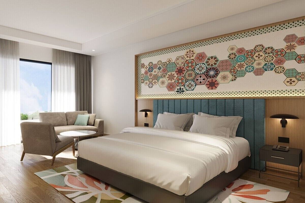 A modern hotel room with a large bed, a sofa, a small round table, and a decorative wall panel.
