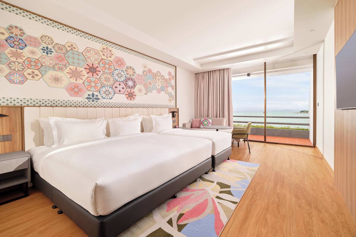 A modern hotel room with a large bed, a balcony with a view of the sea, and a decorative wall.