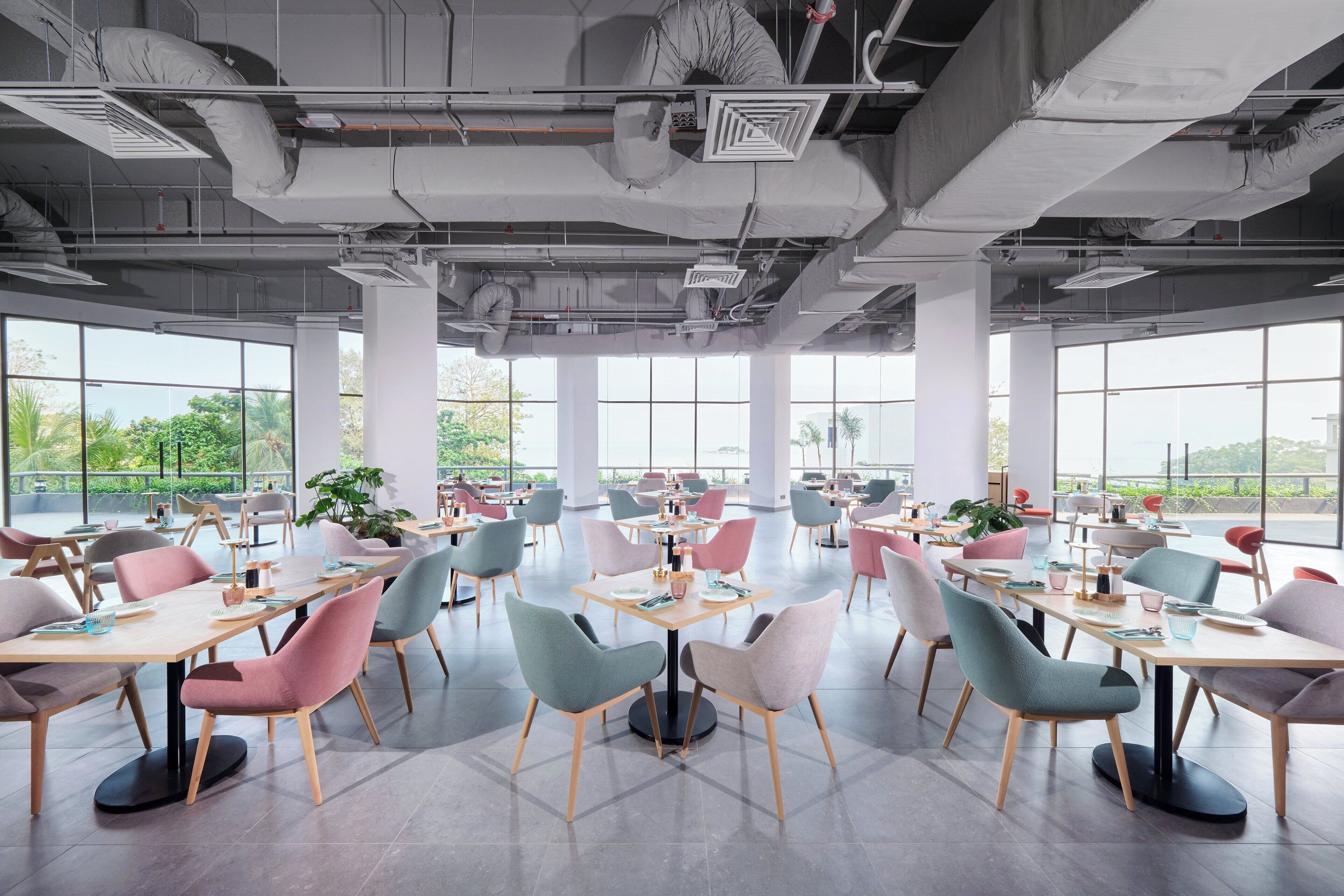 A spacious dining area with multiple tables and chairs, large windows, and visible ceiling ducts.