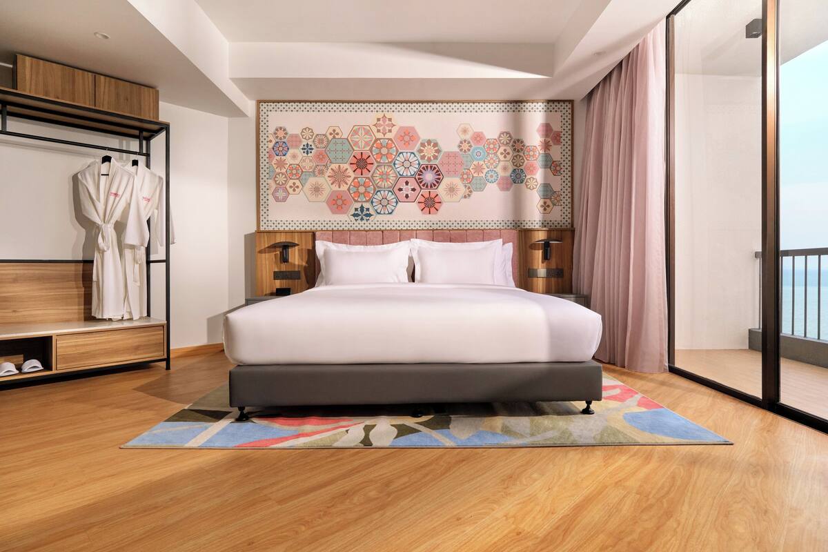 A modern bedroom with a large bed, a wooden wardrobe, a robe rack, and a decorative wall tapestry.