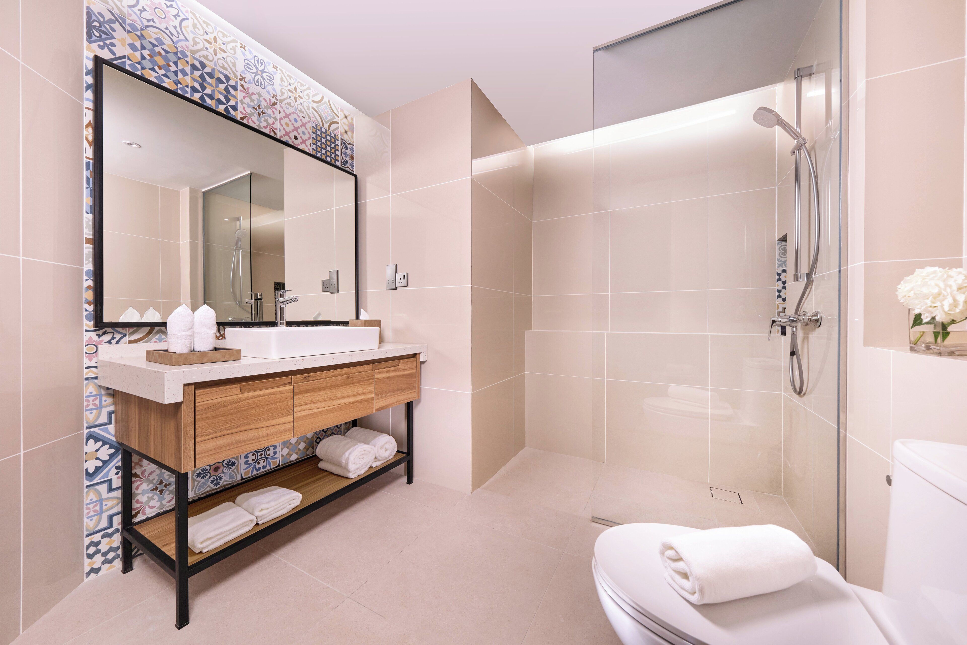 Un baño moderno con un espejo grande, un tocador de madera, una ducha y un inodoro.