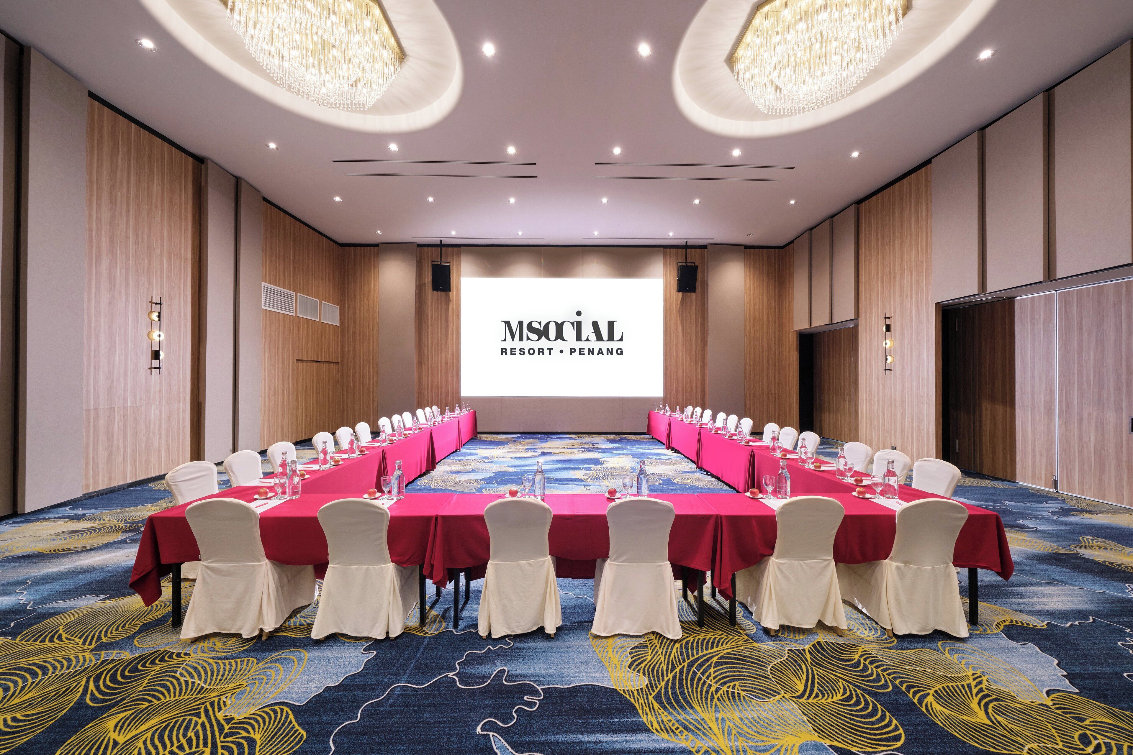 A conference room with a long table, white chairs, and a large screen displaying "MS SOCIAL RESORT PENANG".