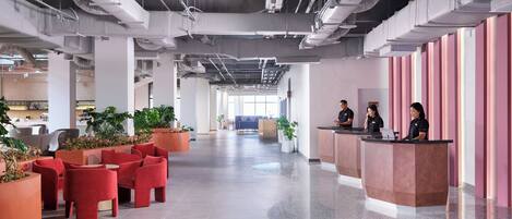 A spacious lobby with red seating, a reception desk, and potted plants.
