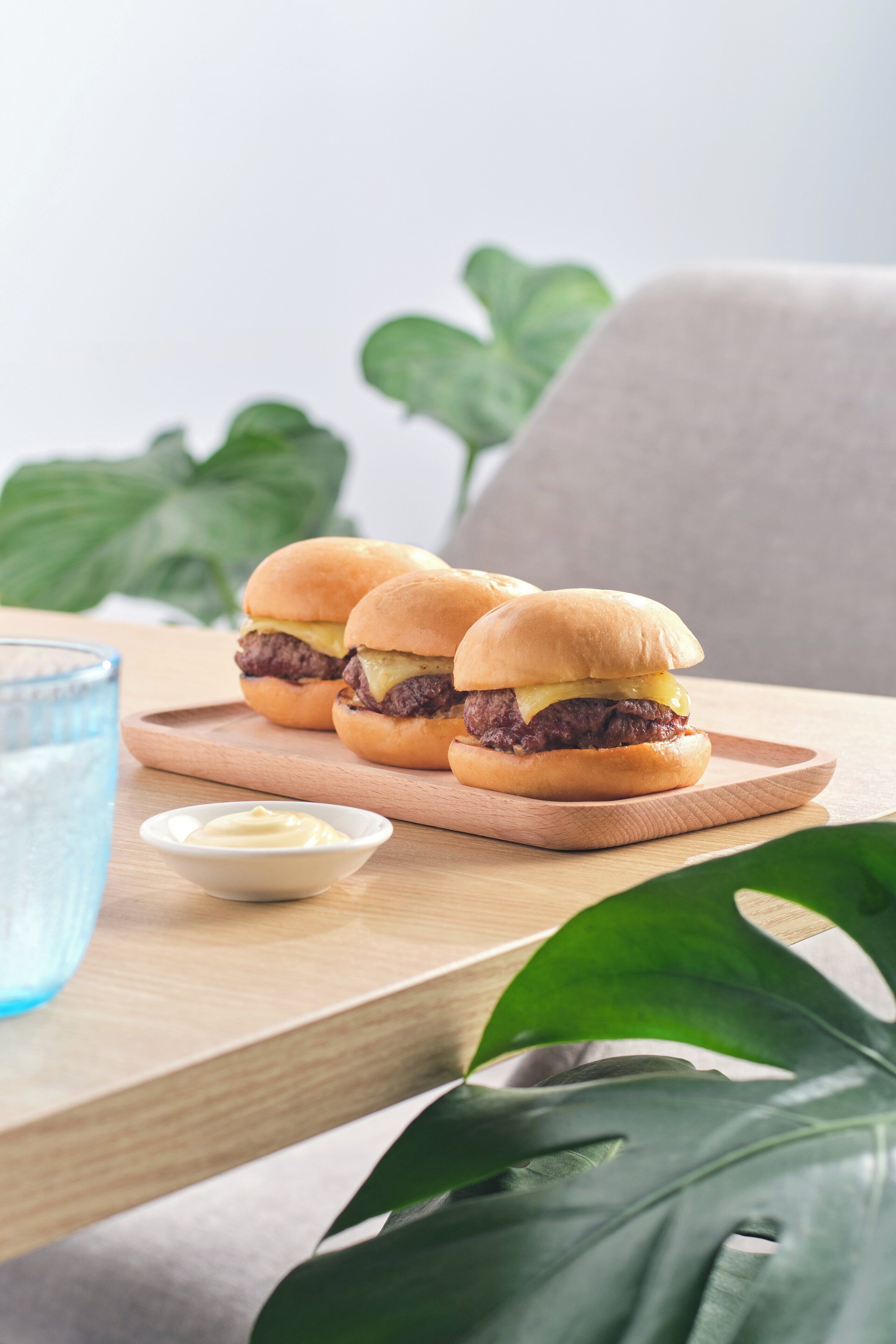 A wooden table with three burgers and a small bowl of sauce.