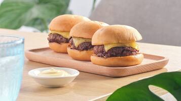A wooden table with three burgers and a small bowl of sauce.