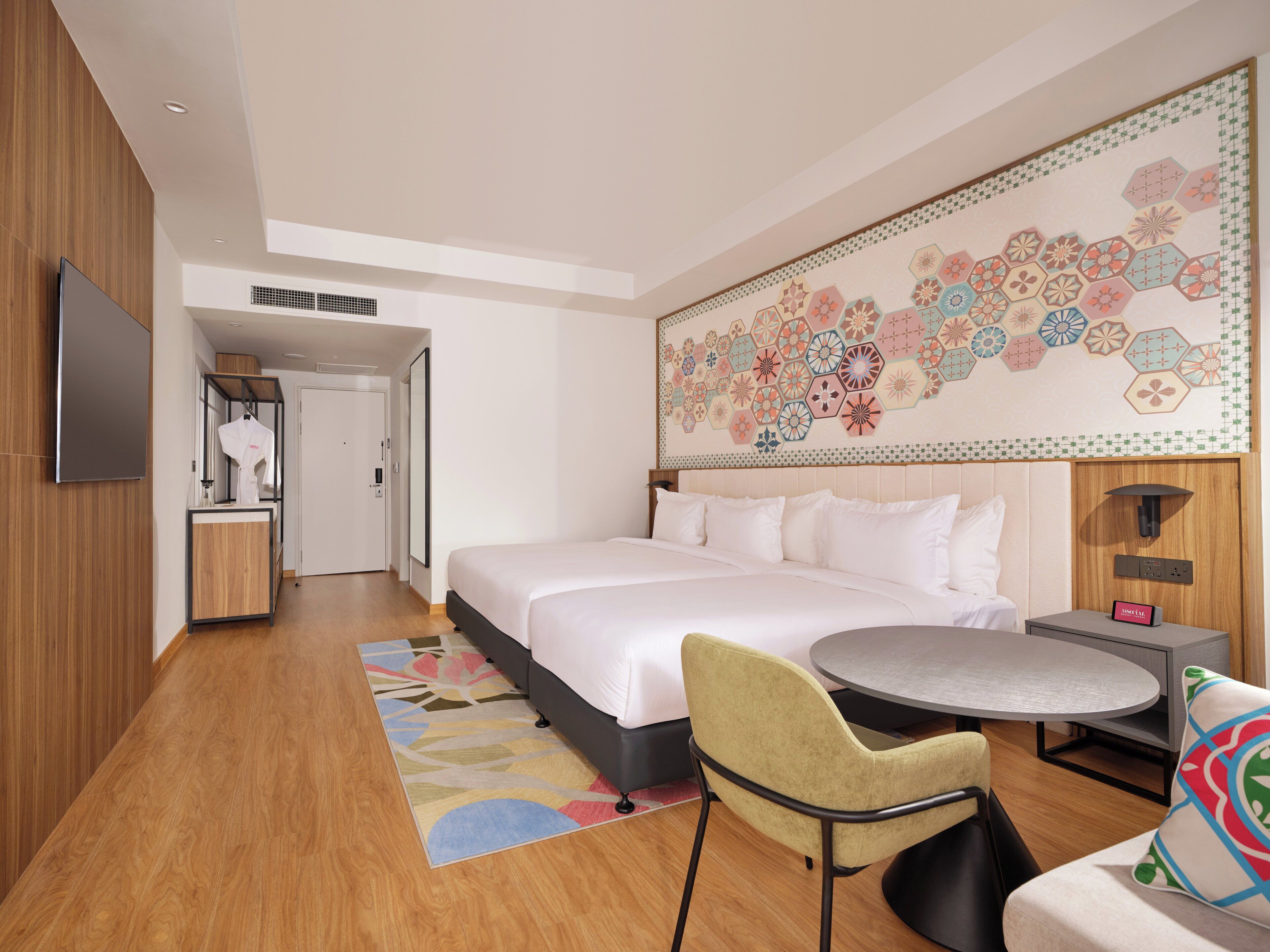 Una habitación de hotel moderna con una cama grande, una mesa redonda de comedor, un sofá y un mural decorativo en la pared.