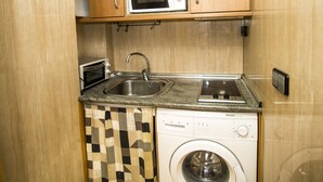 Una cocina compacta con armarios de madera, microondas, tostadora, lavamanos y lavadora.