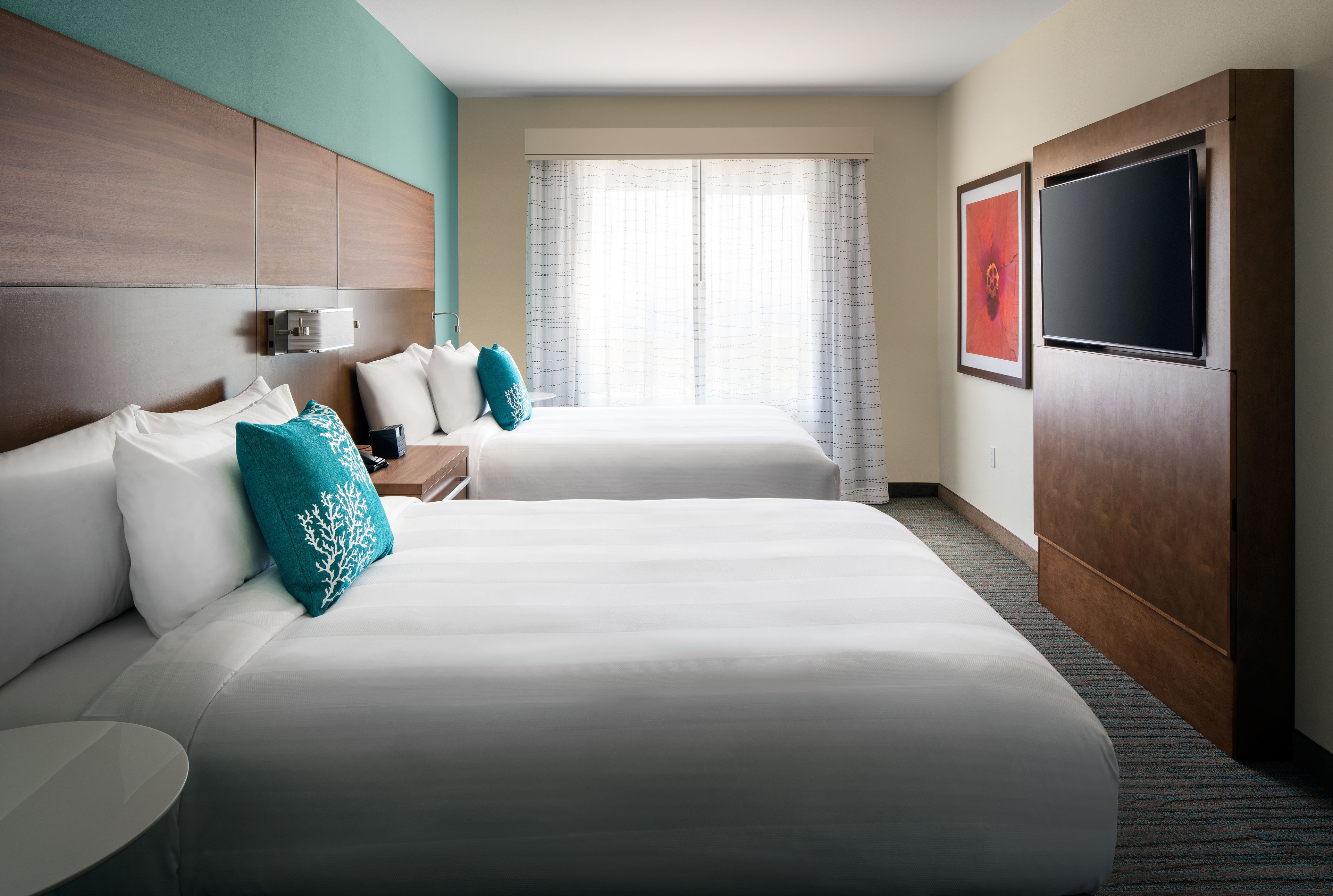 Een hotelkamer met twee bedden, een televisie en een groot raam met gordijnen.