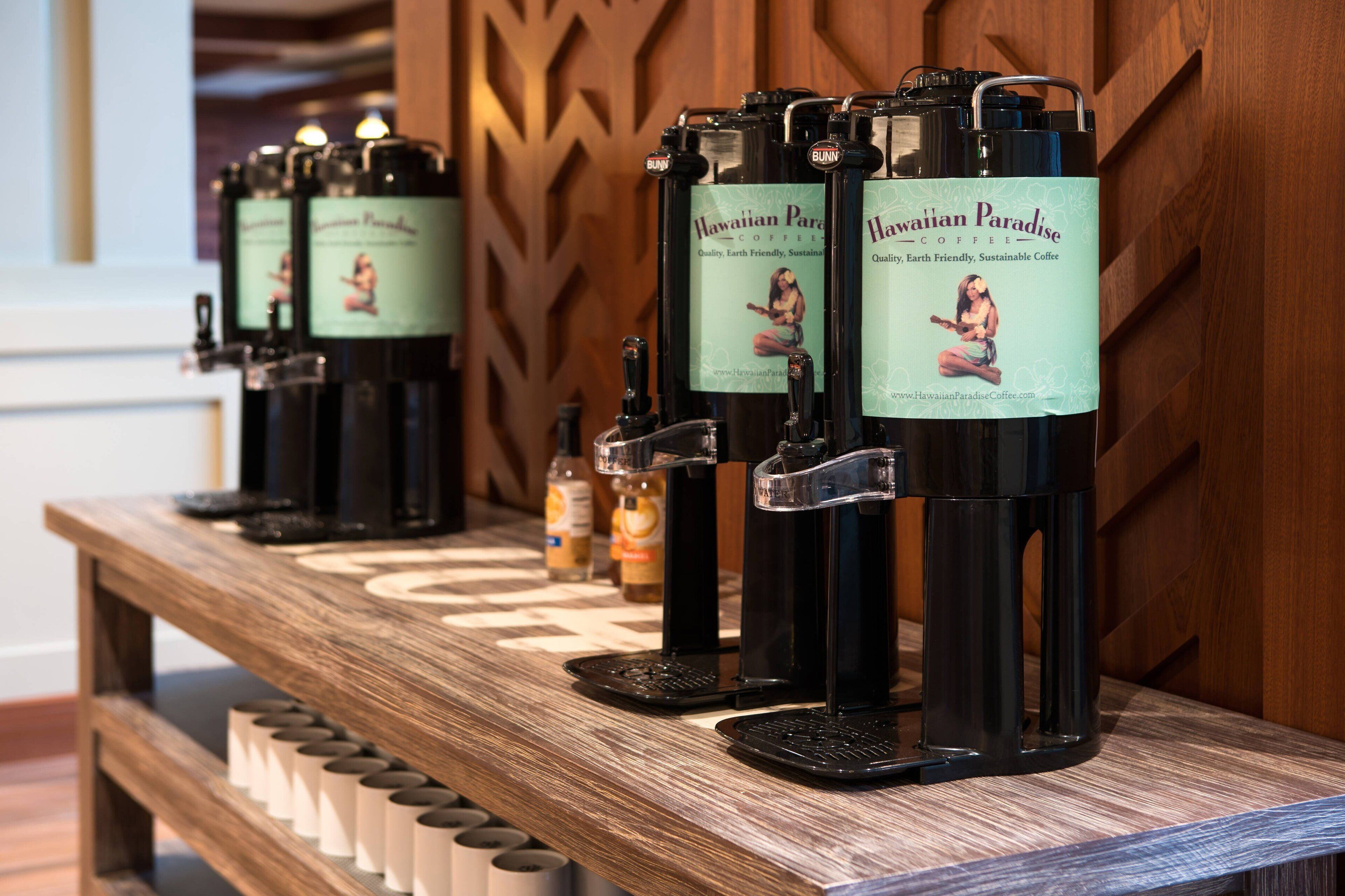 A row of coffee dispensers with labels reading "Hawaiian Paradise Coffee" on a wooden counter.
