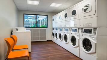 A laundry room with multiple washing machines, a dryer, and two orange chairs.