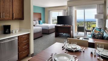 Habitación de hotel con comedor, televisor y balcón con vistas.