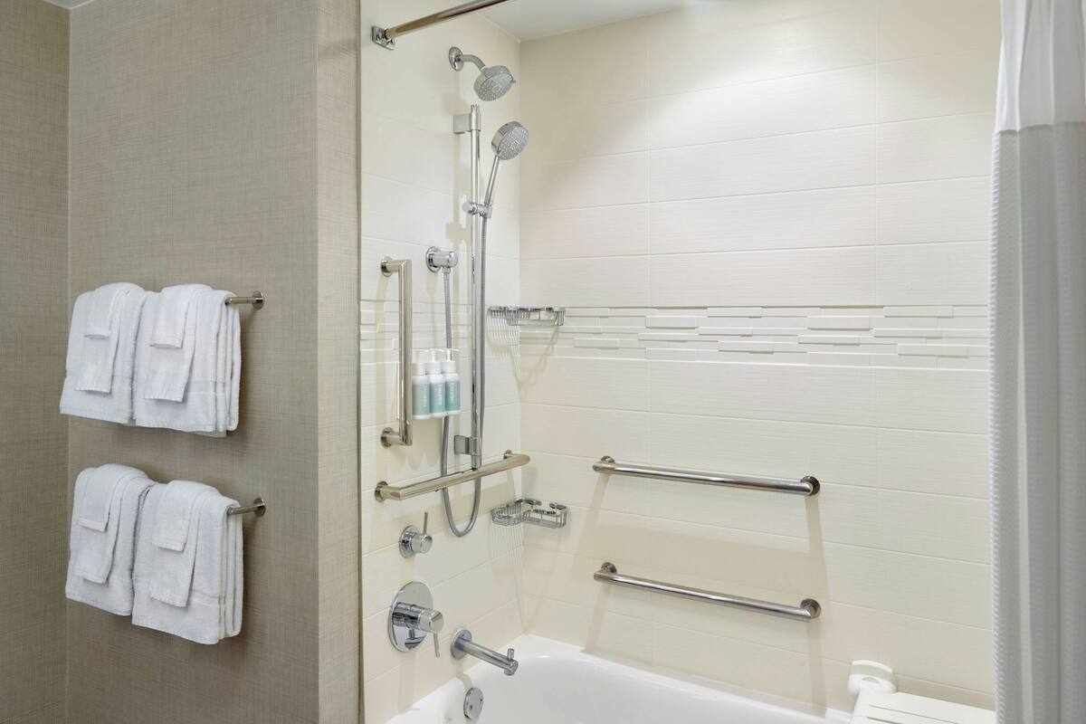 A modern bathroom with a bathtub, shower, and handrails.