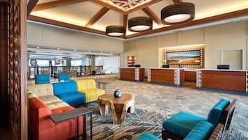A spacious lobby with a reception desk, colorful seating, and a patterned ceiling.