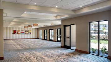 A spacious hotel lobby with a patterned carpet, large windows, and a ceiling with recessed lighting.