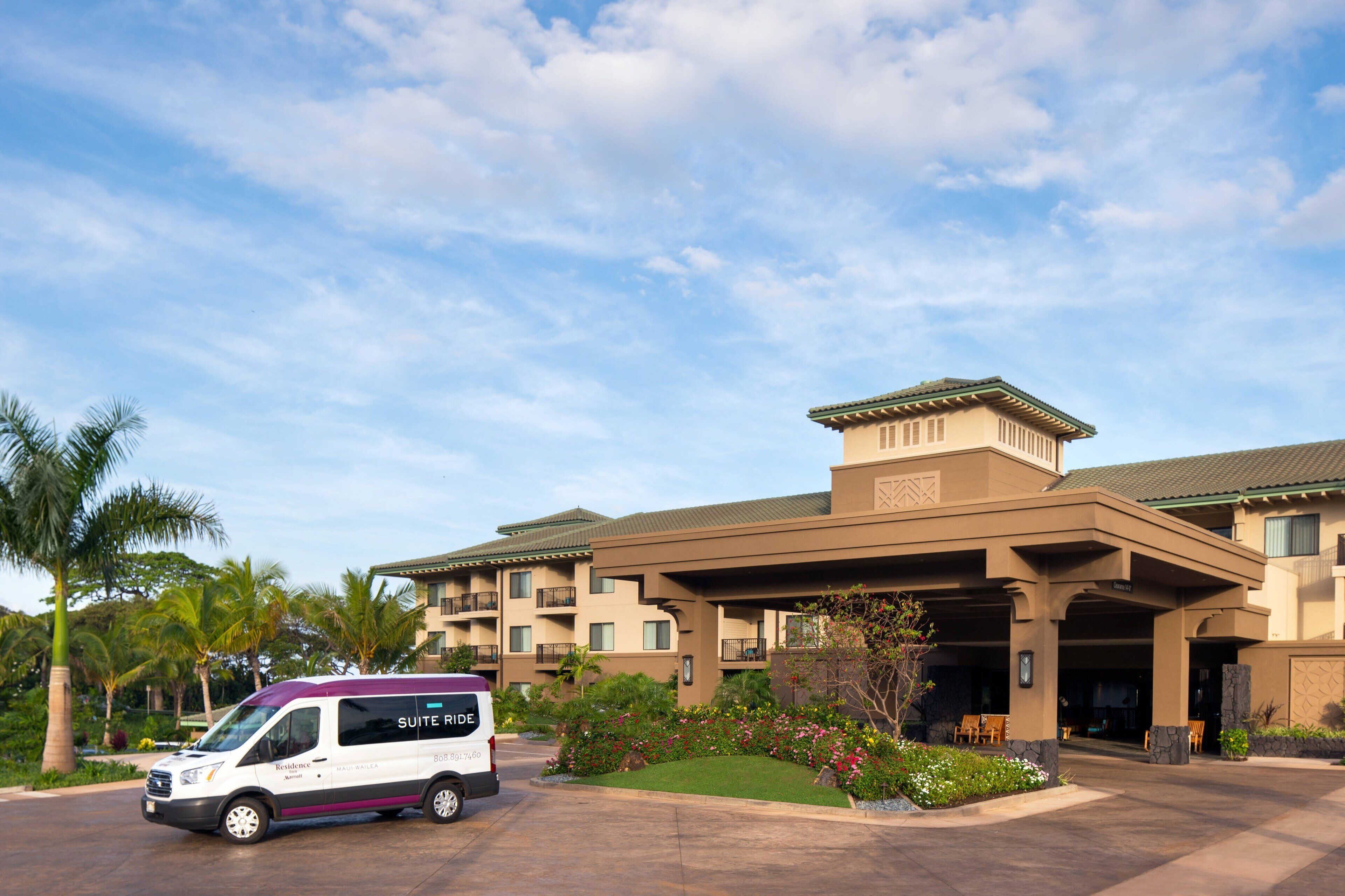 A hotel with a covered entrance, palm trees, and a van labeled "Suite Ride."
