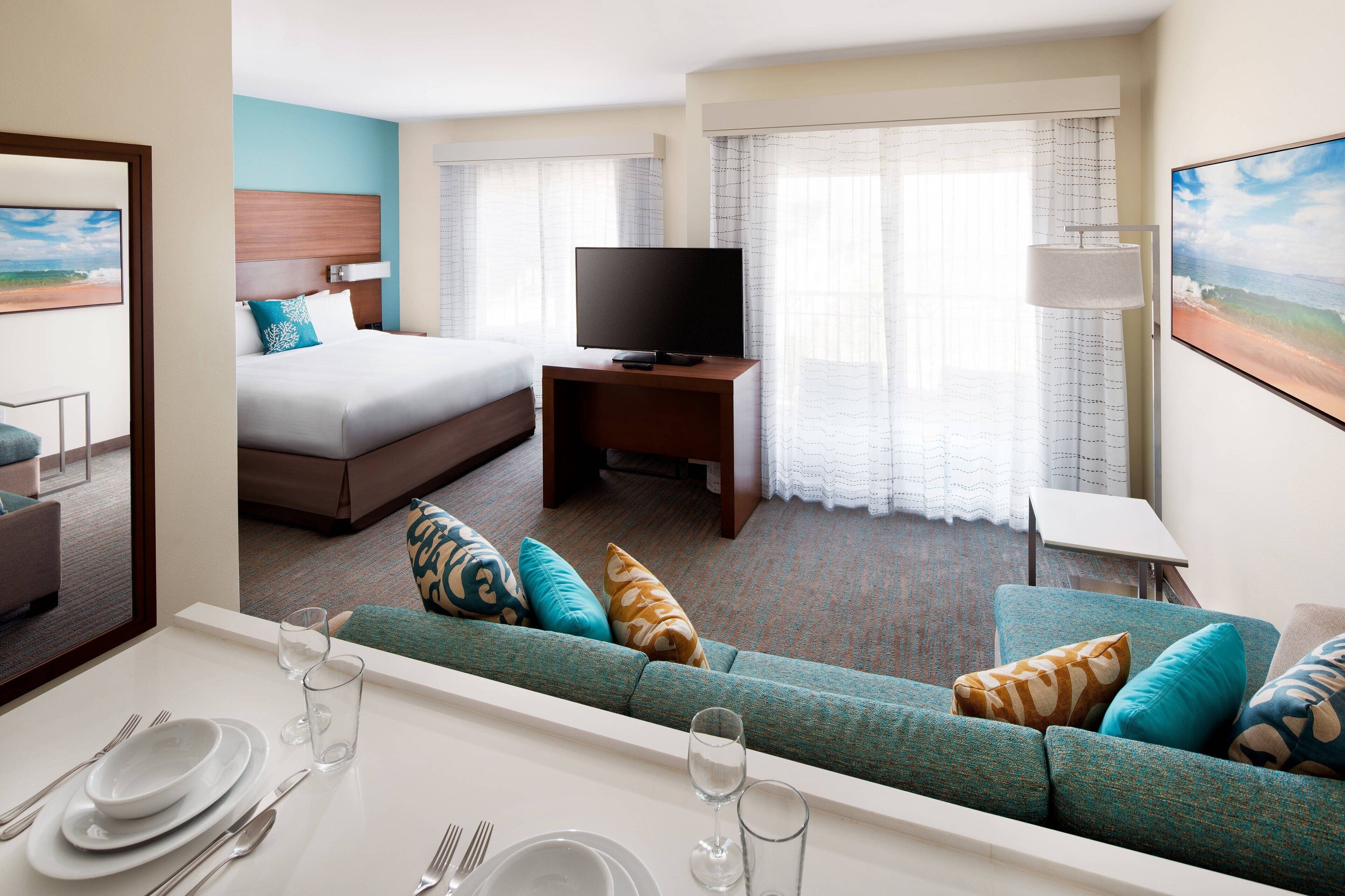 A hotel room with a bed, a TV, a sofa, and a dining area with a table set for two.
