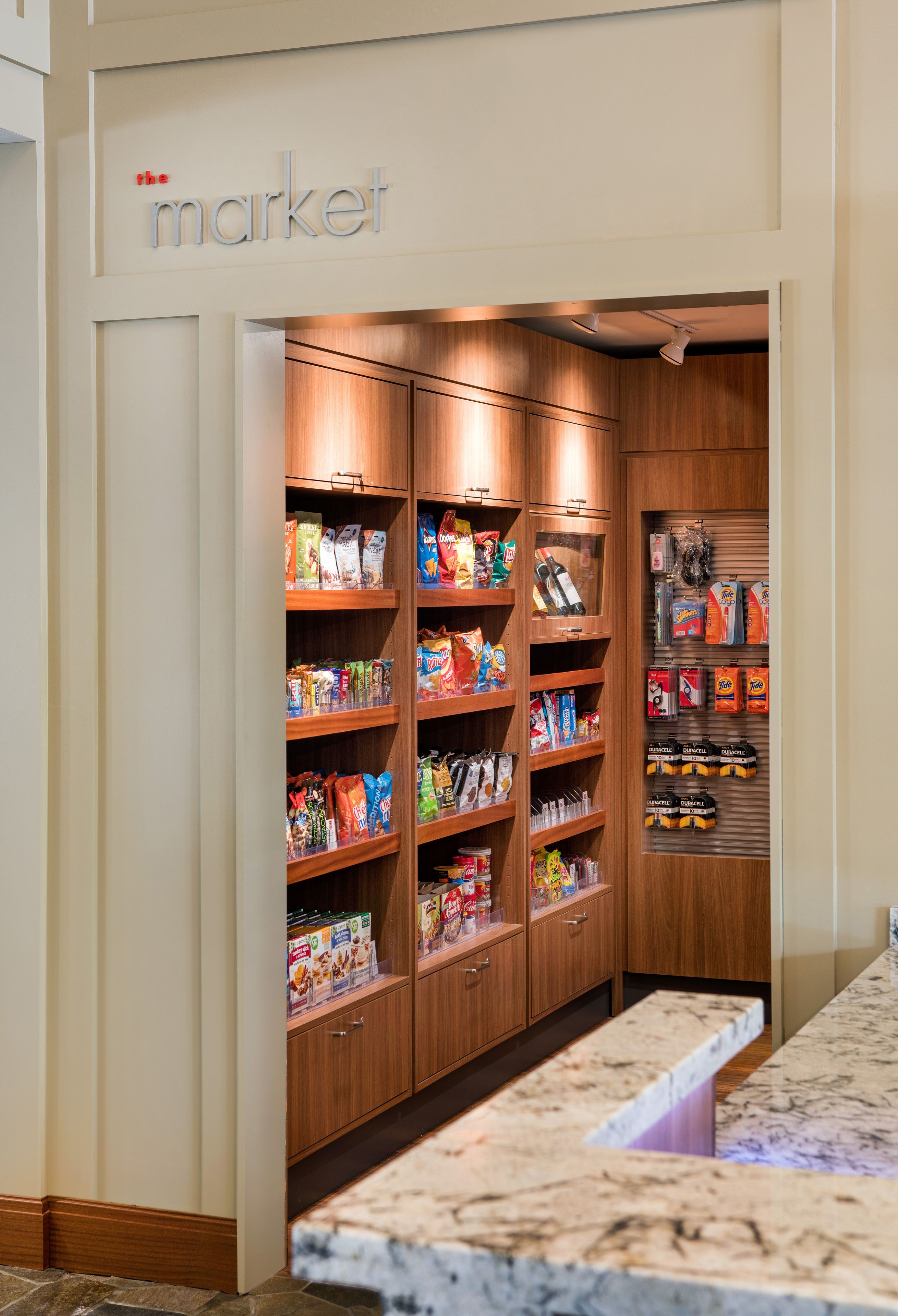 A store with shelves stocked with snacks and beverages, a marble counter, and a sign above reading "the market".