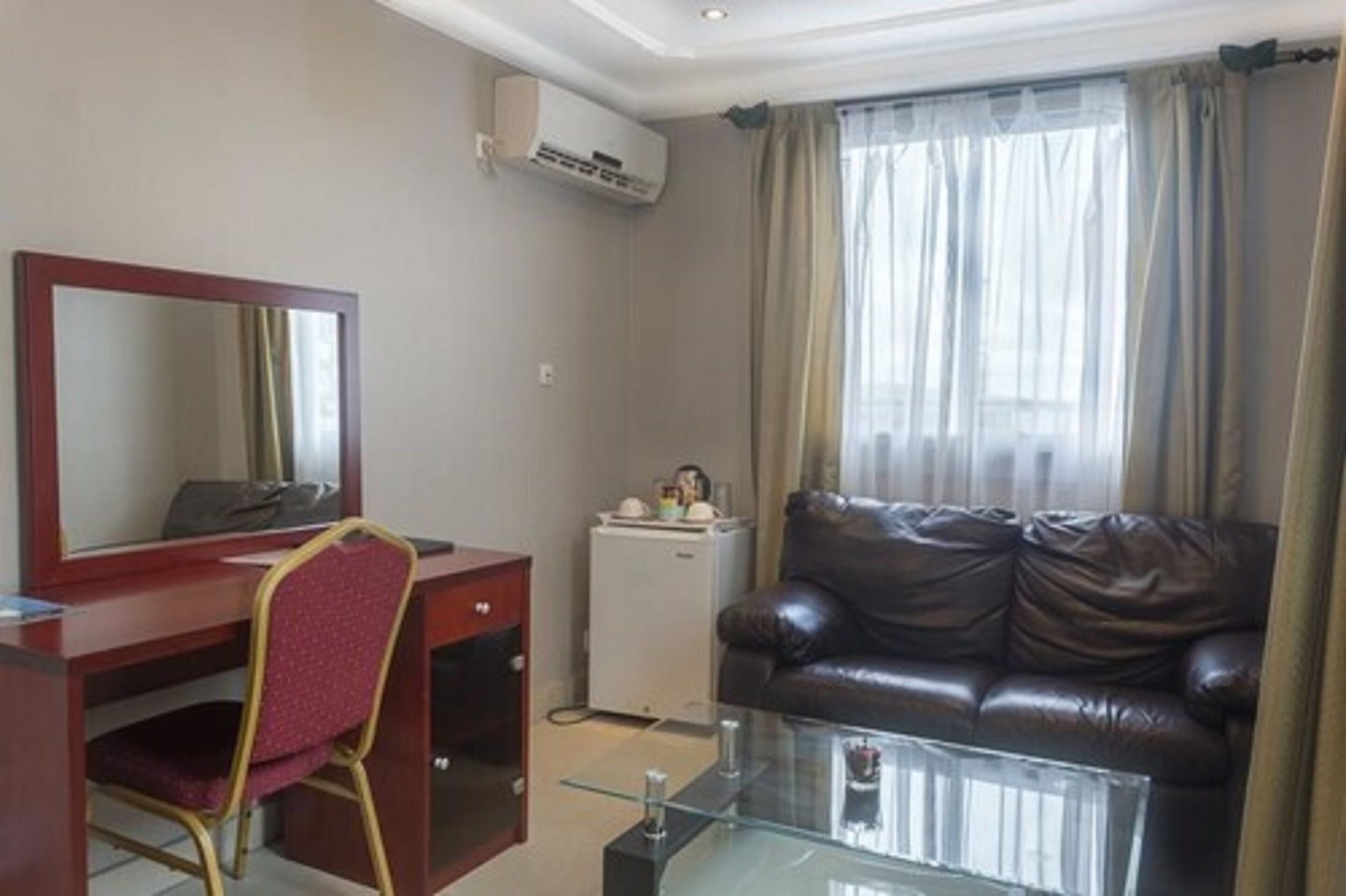 A compact room with a desk, chair, leather sofa, and a glass coffee table.