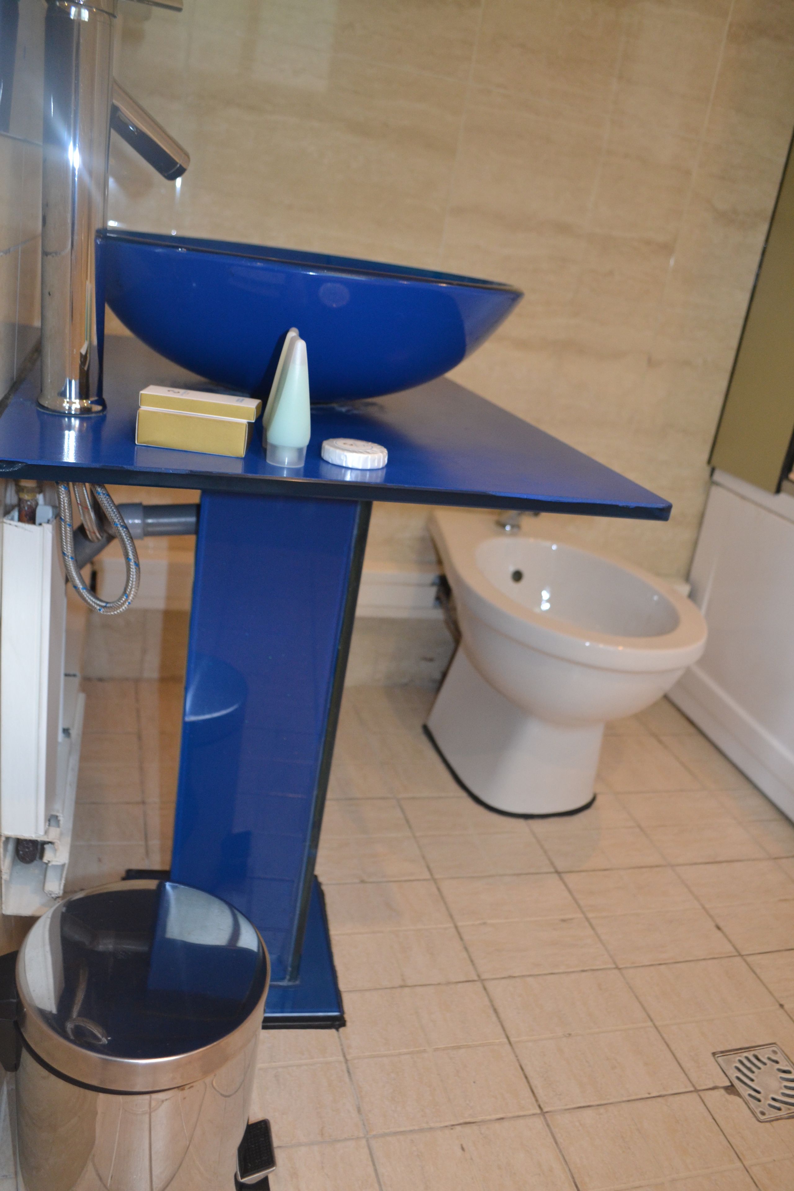 A bathroom with a blue sink, a white toilet, and a trash can.