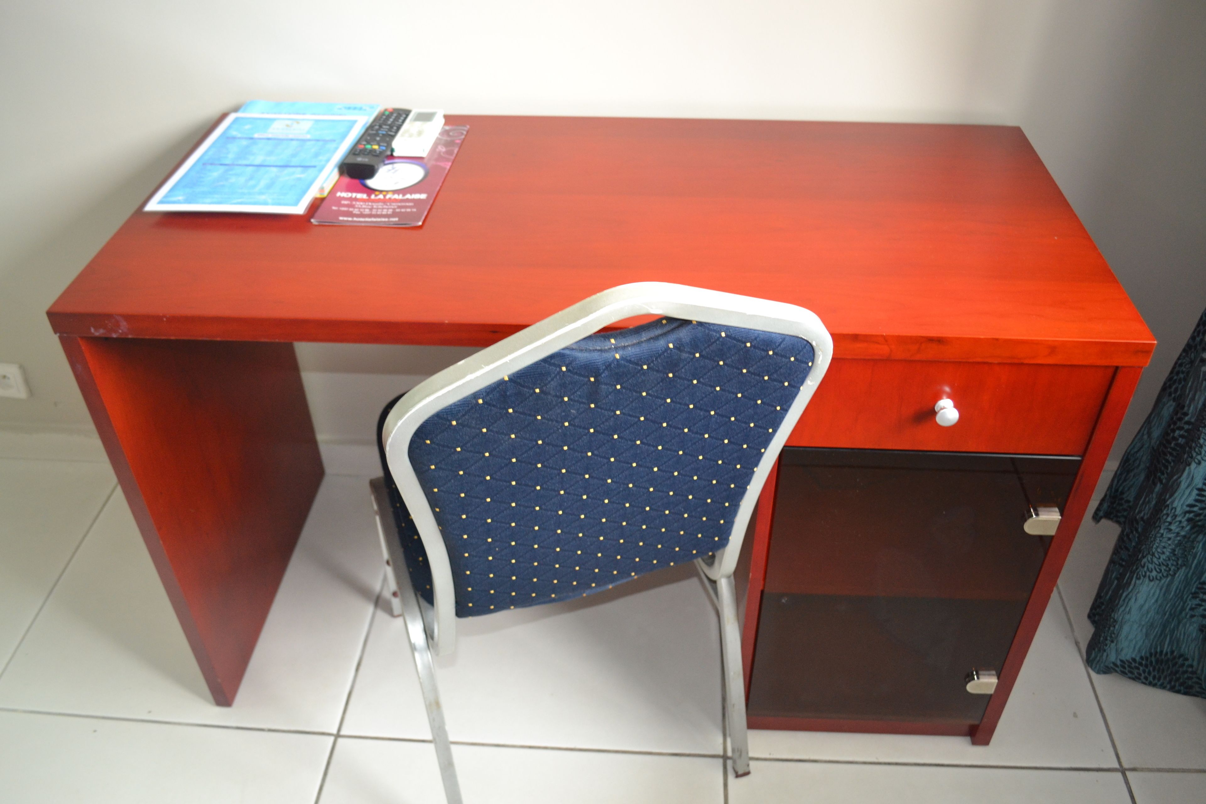 Un bureau rouge avec une chaise bleue, une télécommande et une brochure d’hôtel posés dessus.