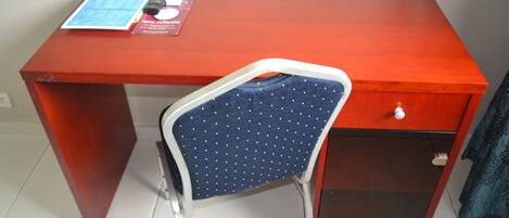 Un bureau rouge avec une chaise bleue, une télécommande et une brochure d’hôtel posés dessus.