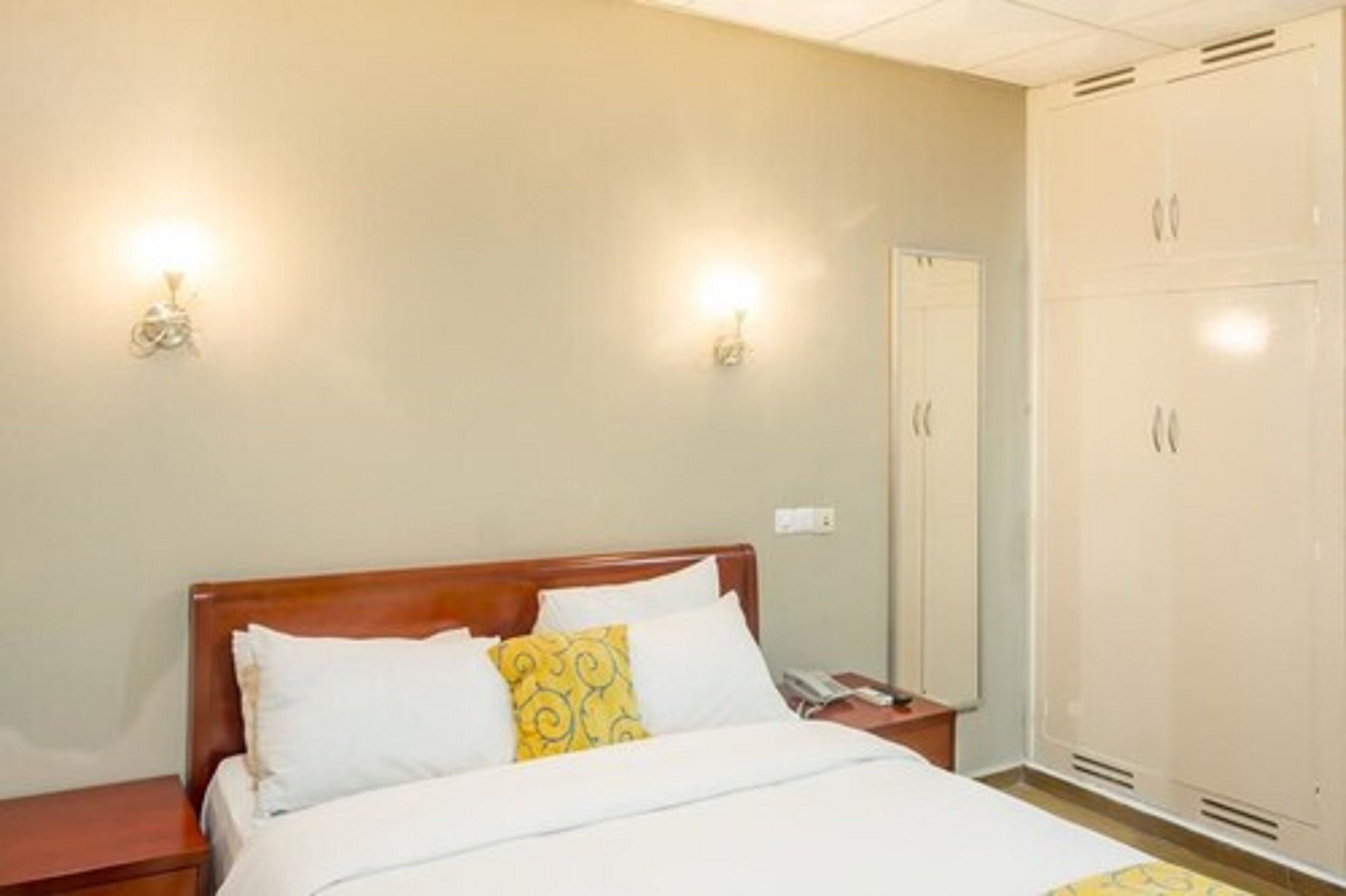 A hotel room with a wooden bed, two wall-mounted lights, a wardrobe, and a bedside table.