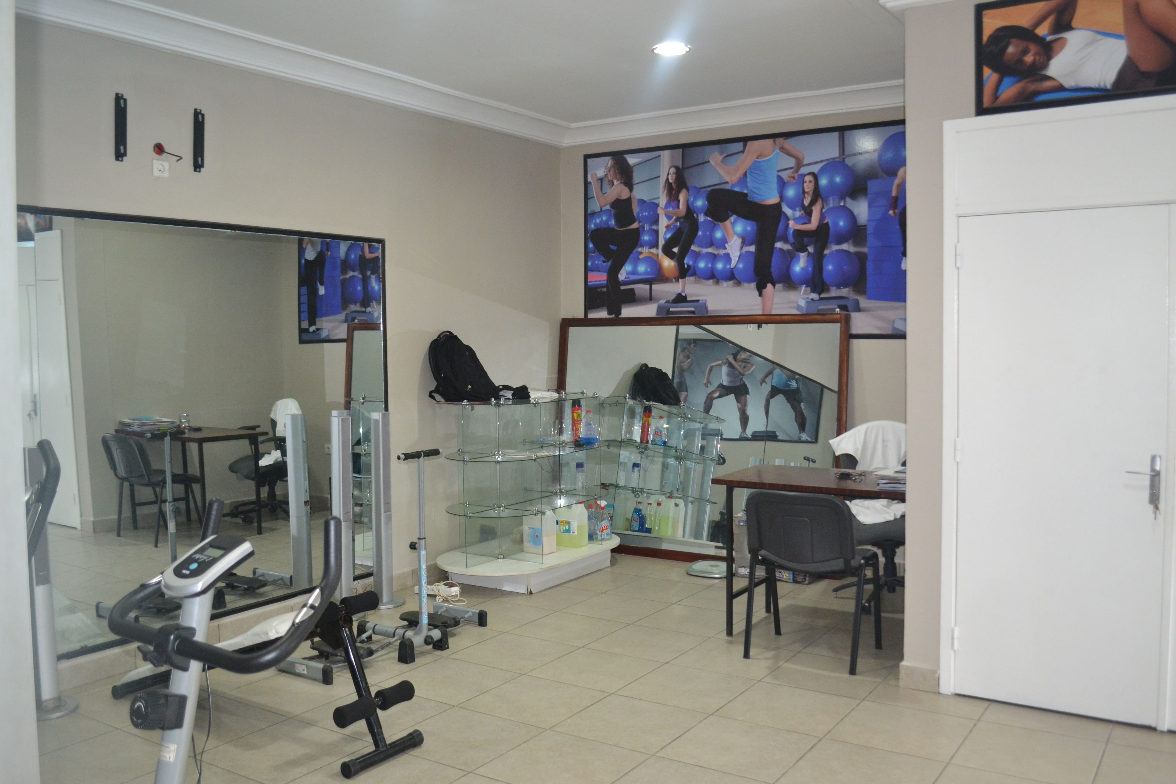Un gimnasio con equipo de ejercicio, un espejo grande y una vitrina con productos.