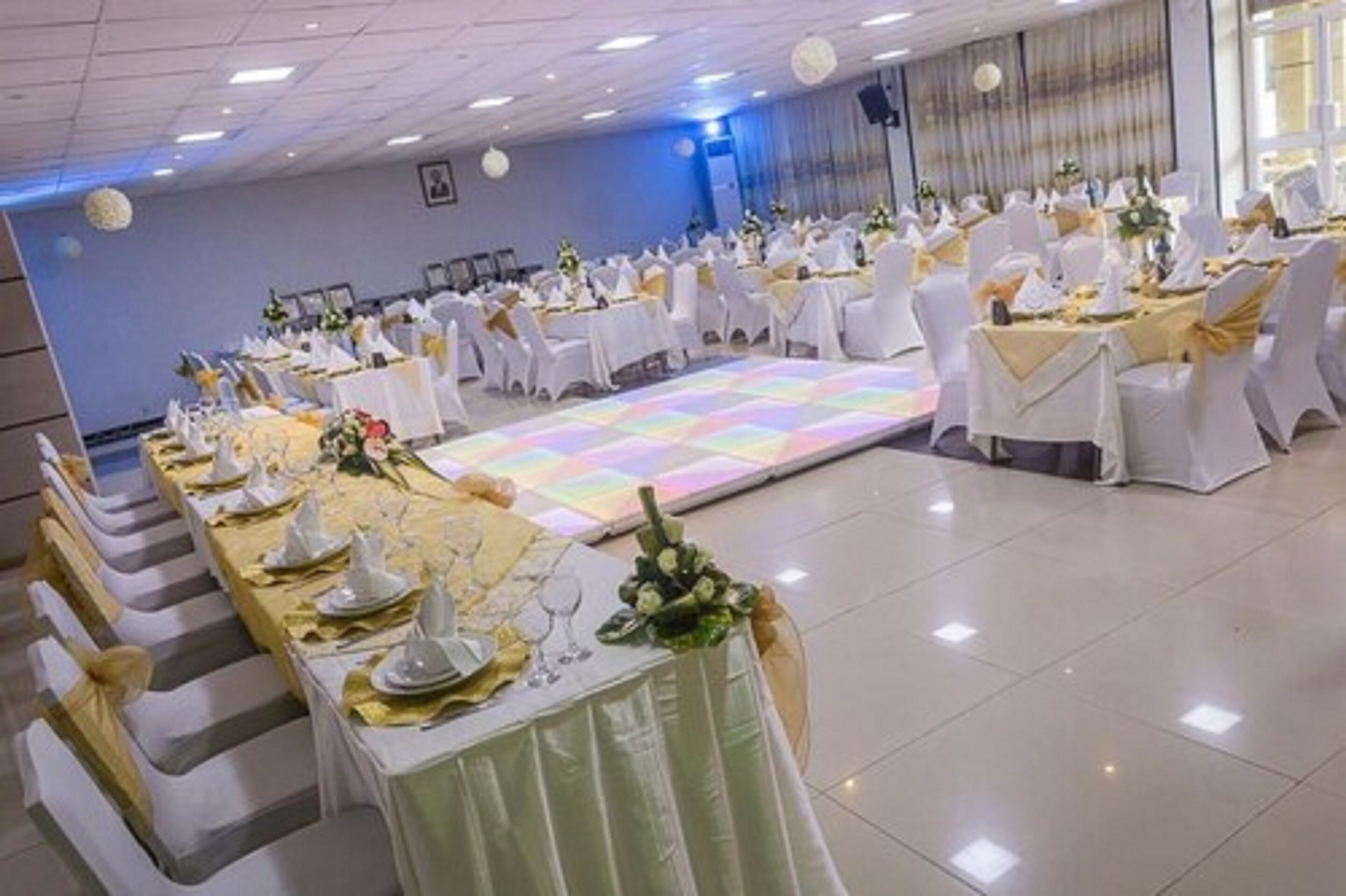 Een feestzaal met ronde tafels gedekt voor een formeel evenement, met witte tafelkleden en gouden accenten.