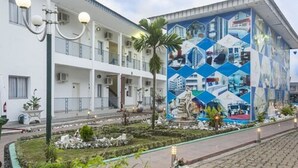 Un bâtiment à la façade blanche, doté d’un balcon et orné d’une fresque aux motifs géométriques.