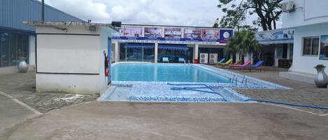 A swimming pool area with lounge chairs and a building with signage.