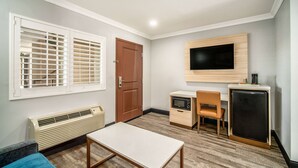 Una habitación pequeña con cama, escritorio, silla, televisor y refrigerador.