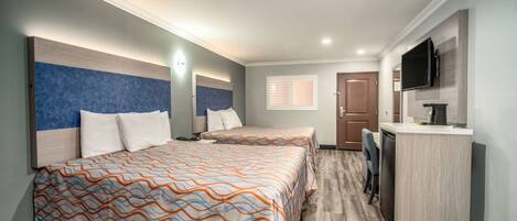 A hotel room with two beds, a desk, a TV, and a window.